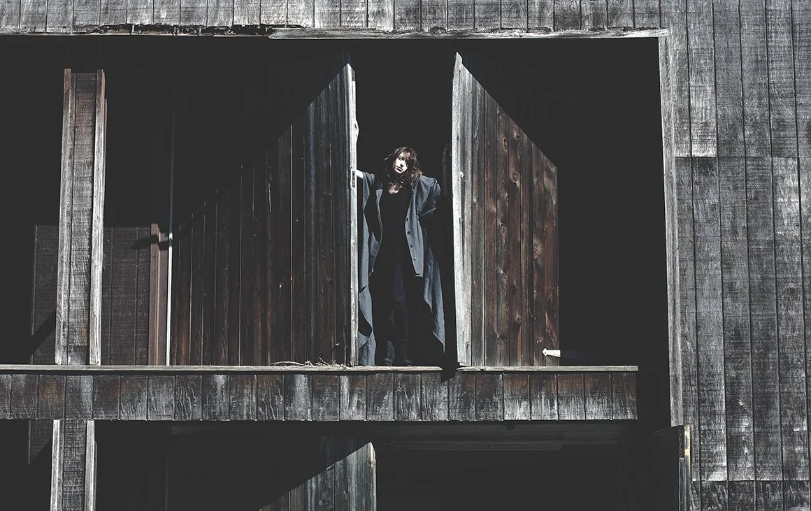 Person standing in an open barn door with wooden exterior