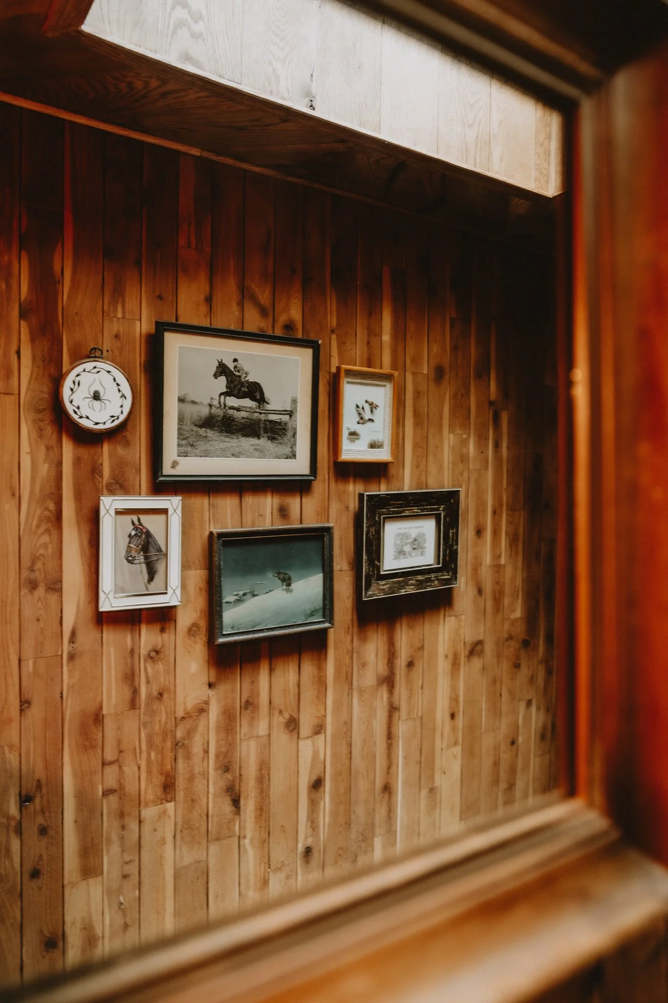 A wooden wall with six framed pictures, including a horse, a skier, and ducks.
