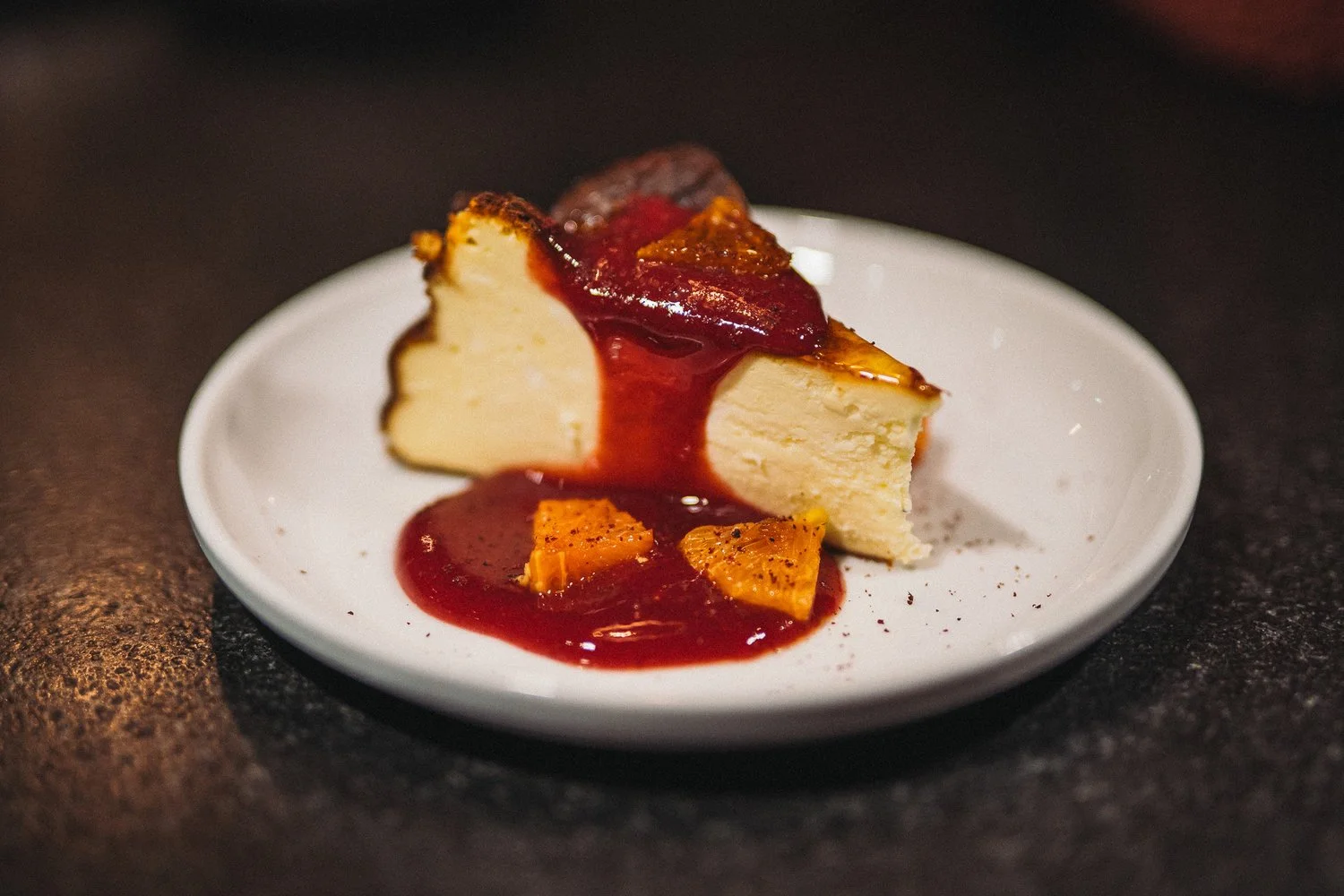 Cheesecake topped with red fruit sauce and garnished with orange pieces on a white plate.