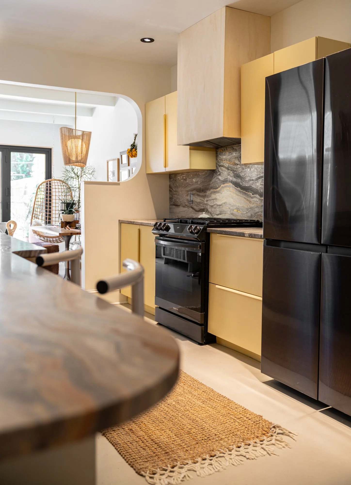 Modern kitchen with black refrigerator, yellow cabinets, marble backsplash, black stove, and a woven rug on the floor.