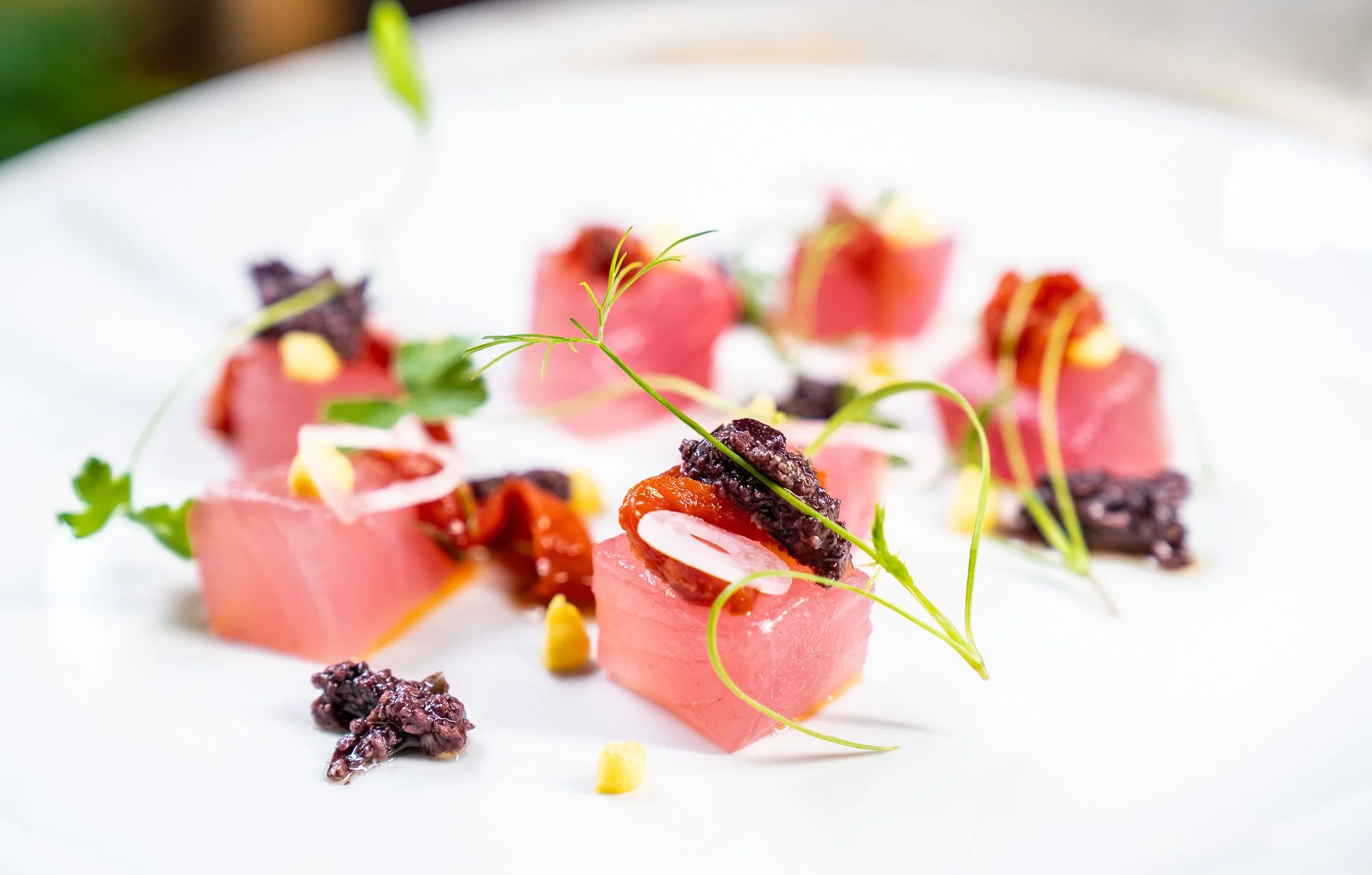 Close-up of finely diced pink tuna sashimi garnished with herbs, black caviar, and small edible yellow or white accents on a white plate