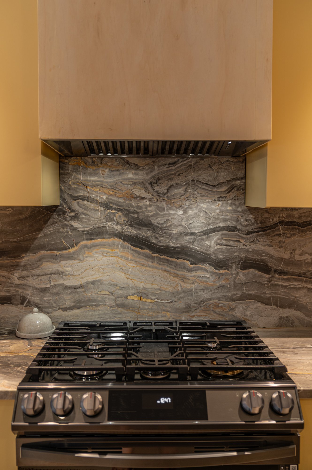 Kitchen stovetop with control knobs, a marble backsplash, and a wooden range hood.
