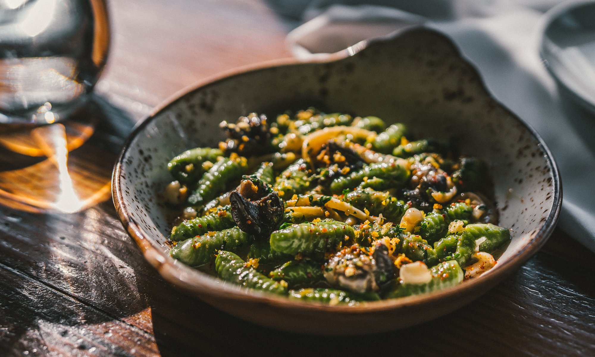 A bowl of green sashimi or vegetable salad on a wooden table with a glass of beverage nearby