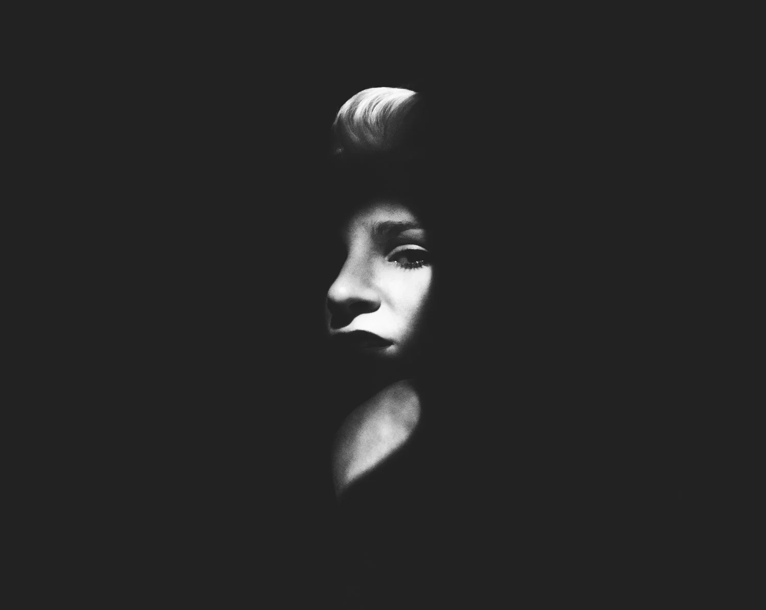 Black and white photo of a woman's face partially illuminated, with a dark background.