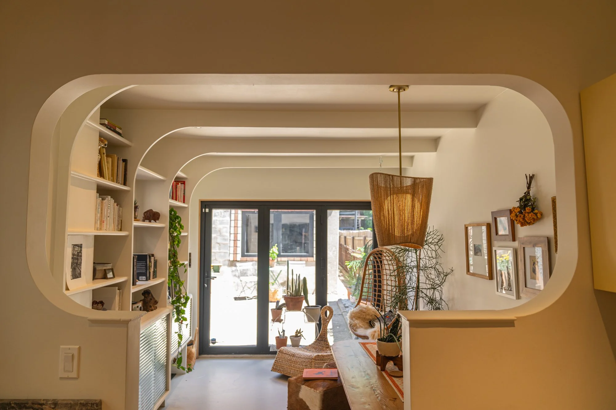 Living room with built-in bookshelves, potted plants, a hanging light fixture, and a sliding glass door leading to an outdoor patio.