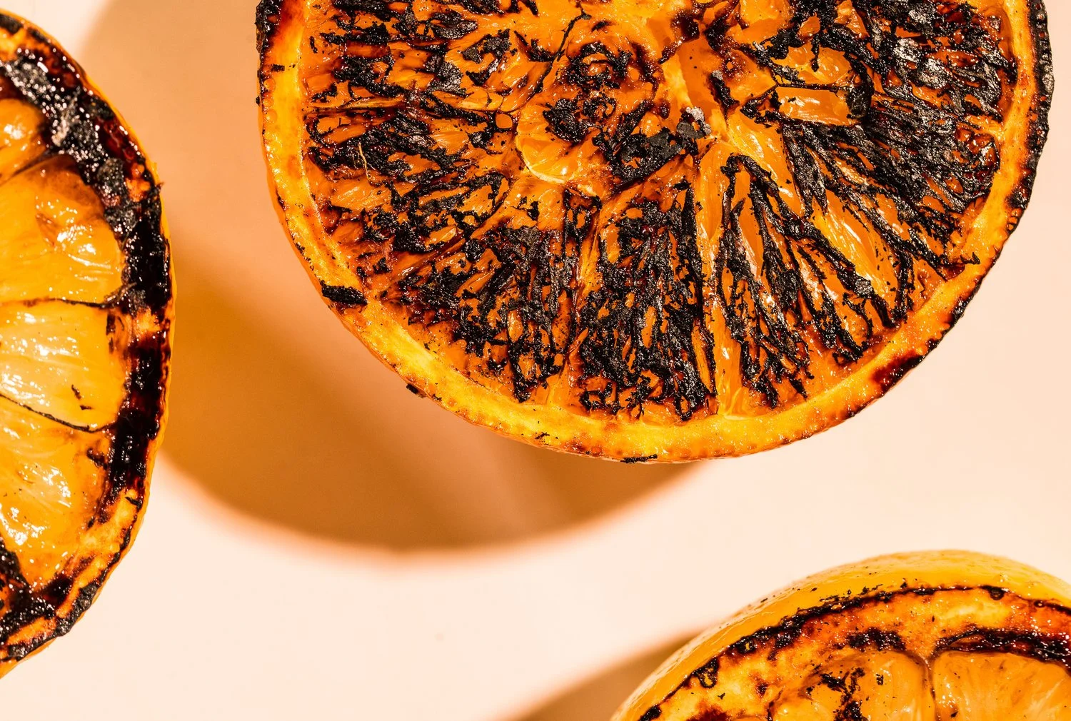 Close-up of grilled orange halves with charred black markings on the juicy flesh.