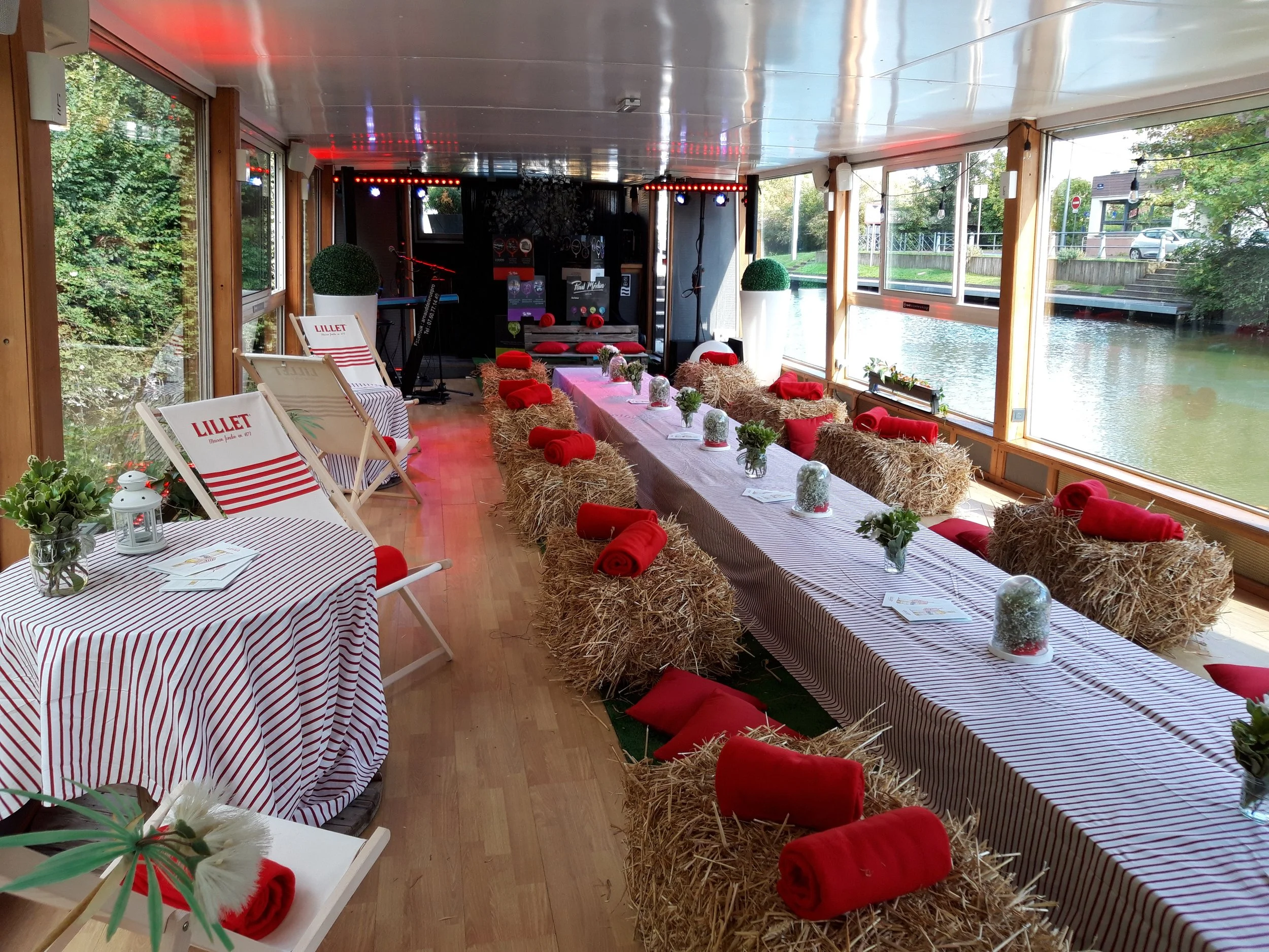 Salle vitrée de L’Eldorado dressée pour un repas champêtre, bottes de paille et coussins rouges