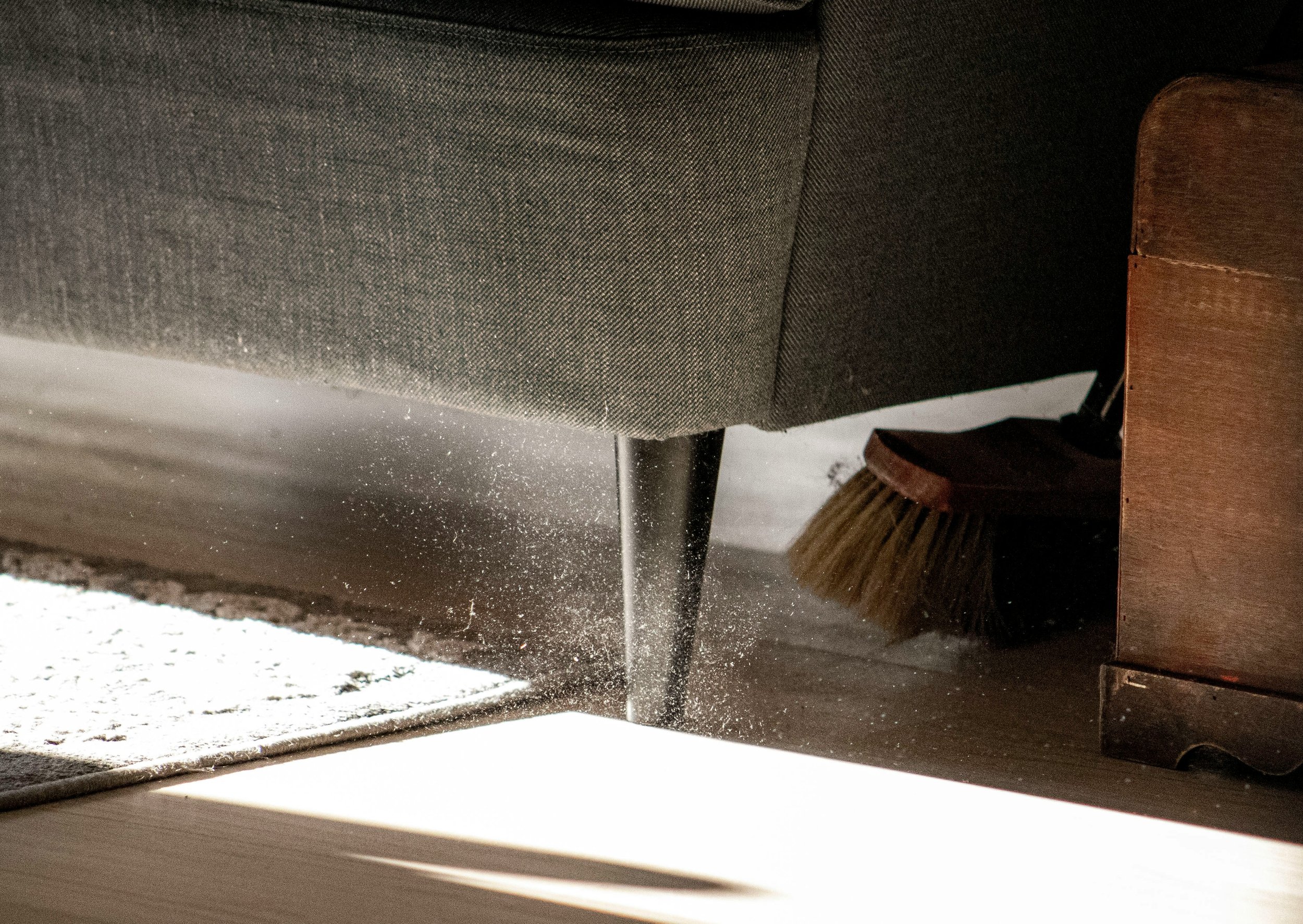 A close up of a broom sweeping up dust under a chair  on the floor