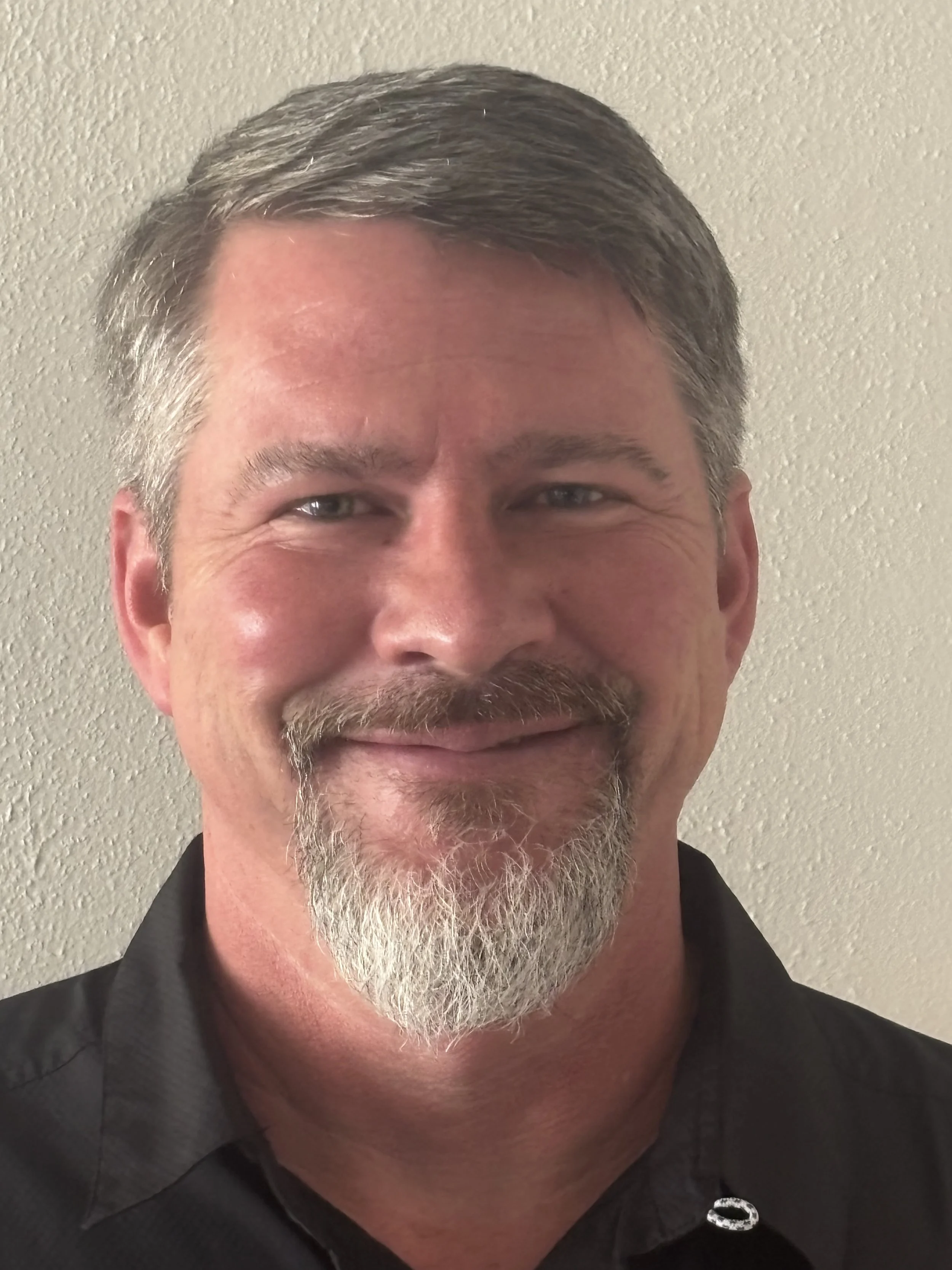 Close-up photo of a smiling man in front of beige wall..
