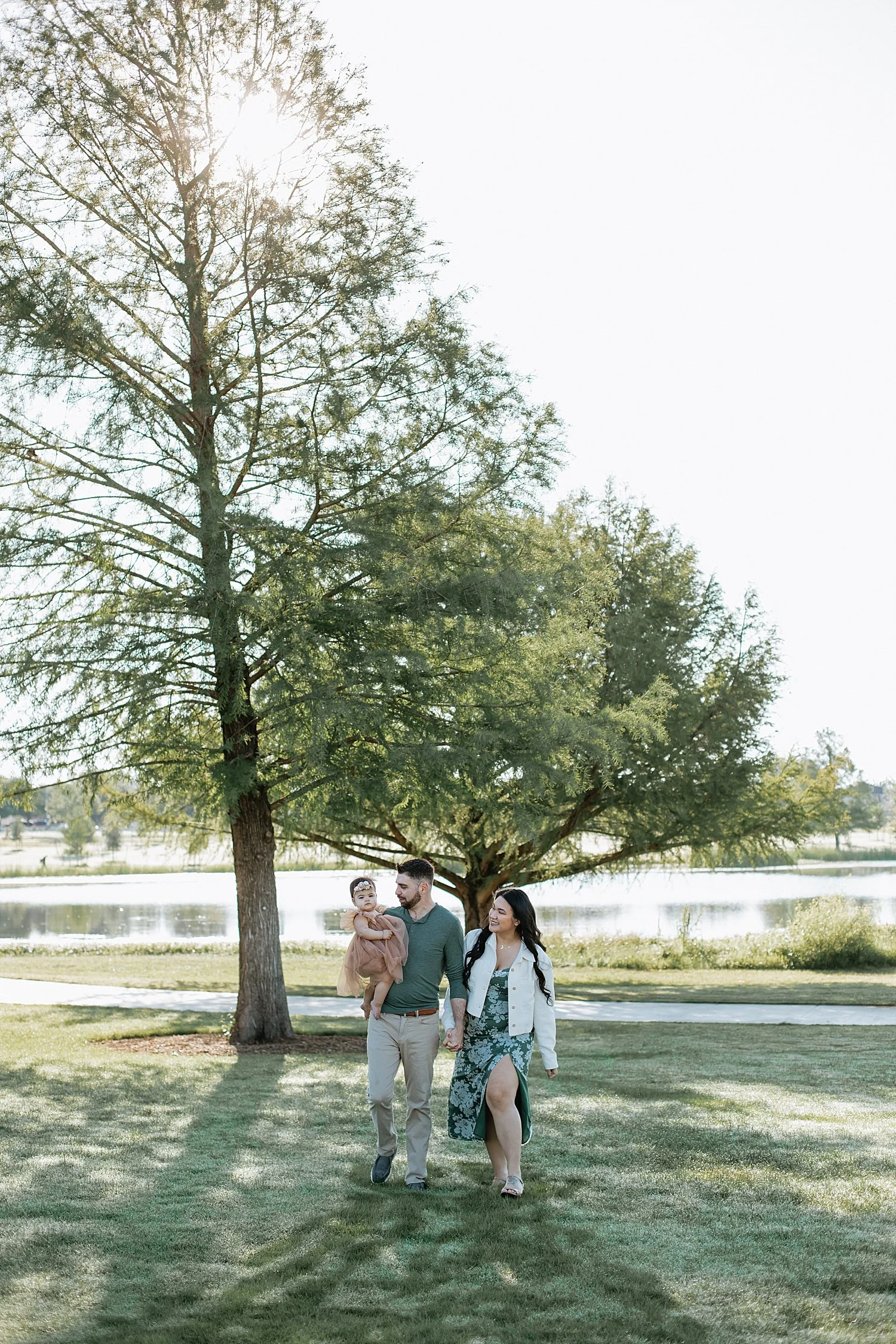 a mom and dad walk with their toddler under a tree for sunrise milestone session