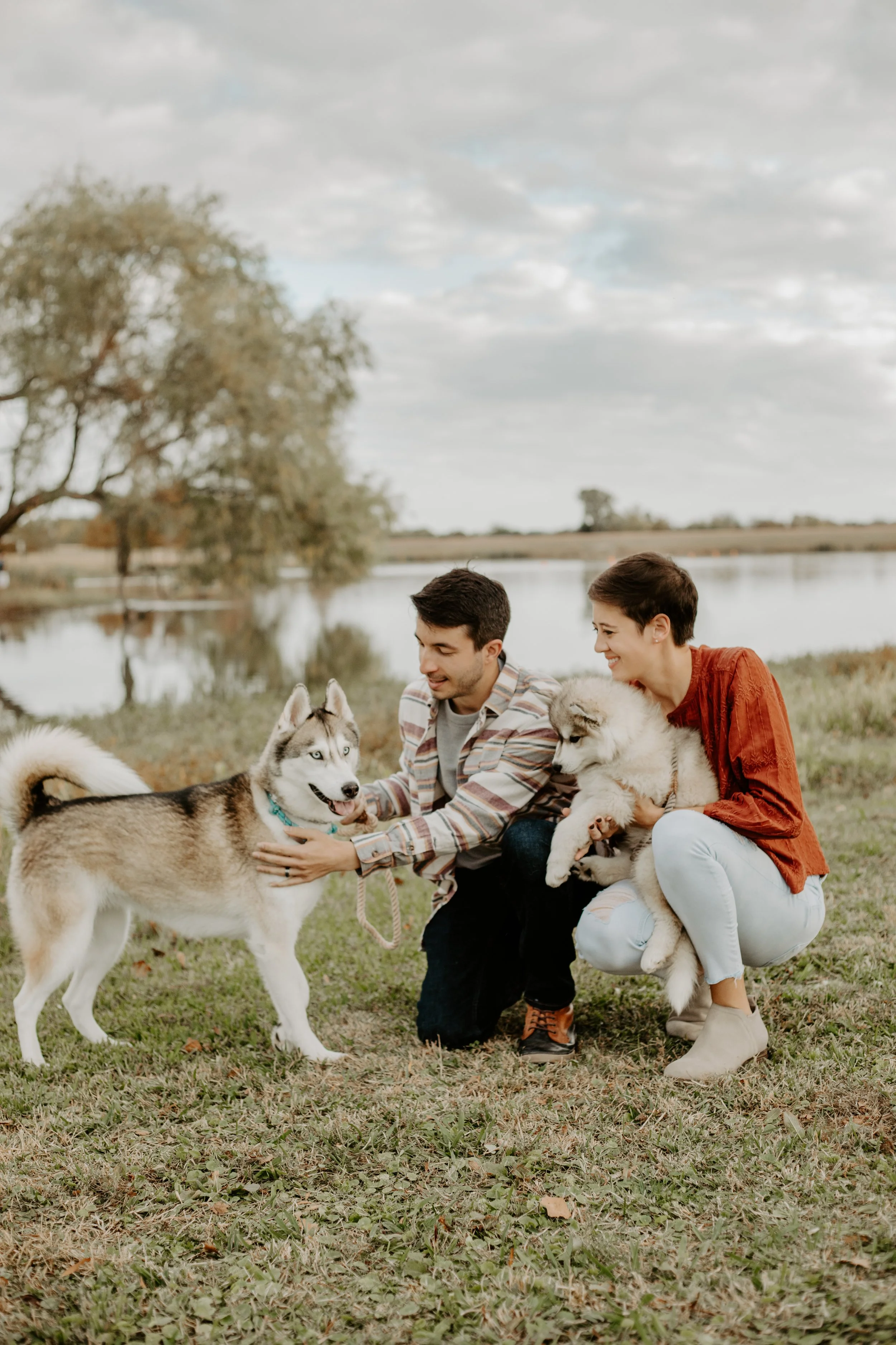 couple kneel down to pet their two huskie puppies for mini sessions