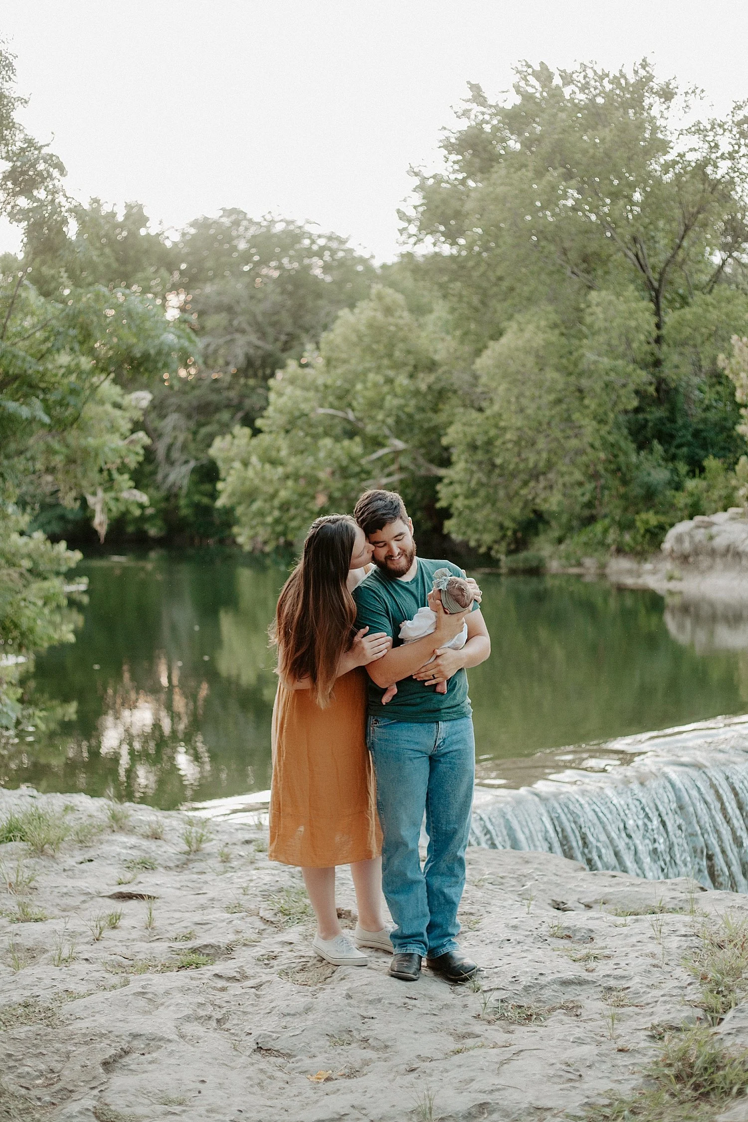 new parents hold baby near waterfall by Austin family photographer