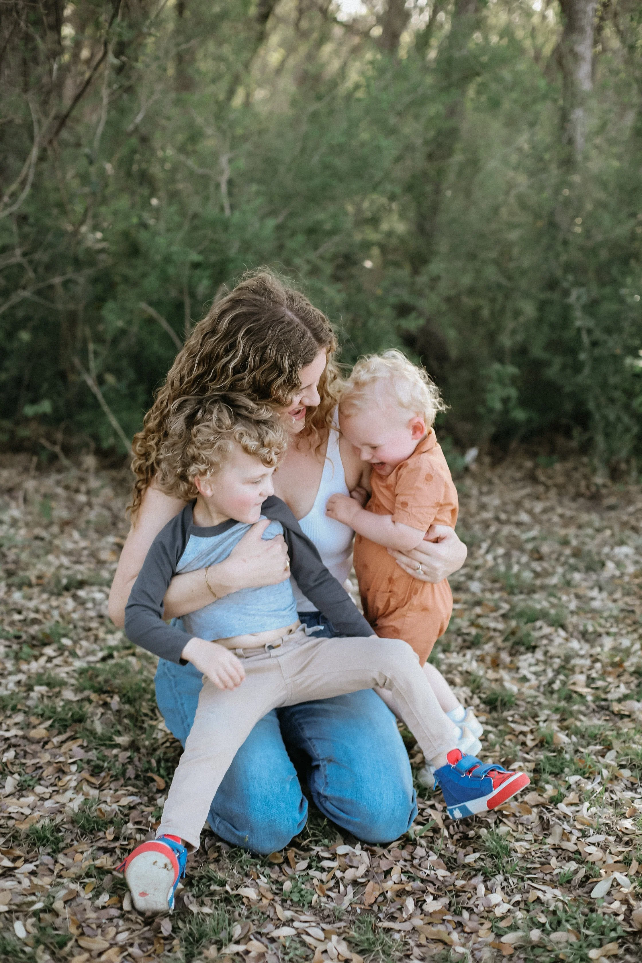 mama snuggles her two toddler boys in grass by Jessie Shaw Photo