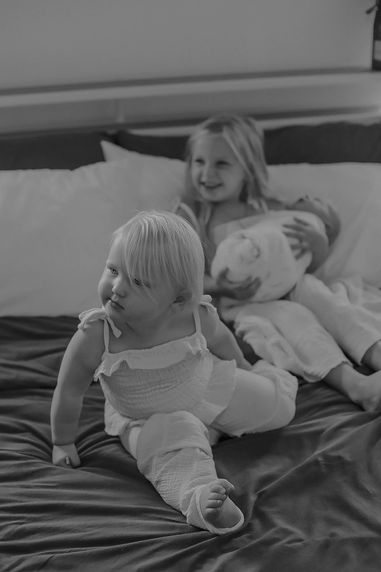 small toddlers sit on the bed with their baby brother for in-home newborn session