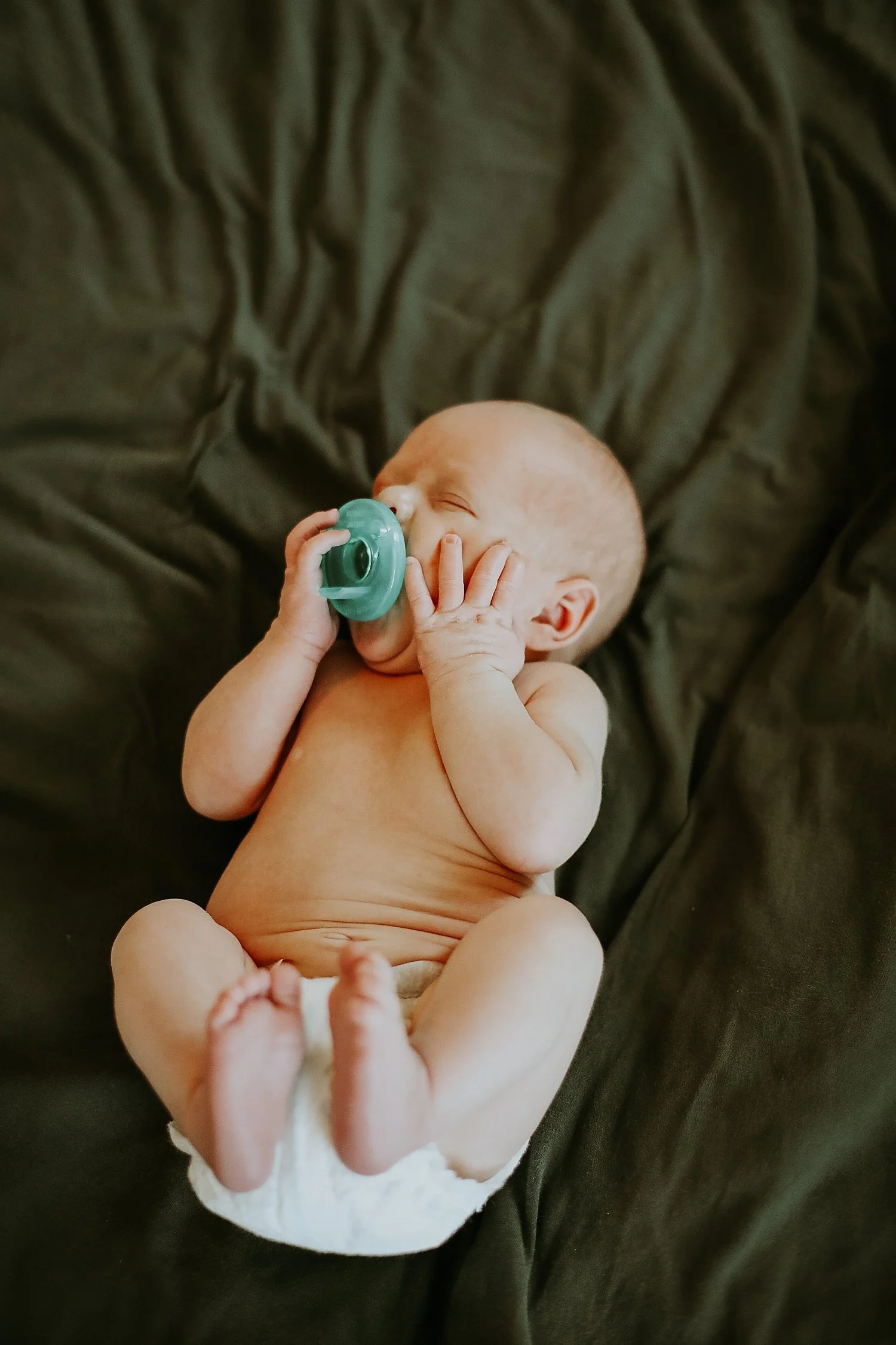 infant holds paci in his mouth lying on bed by Jessie Shaw photo