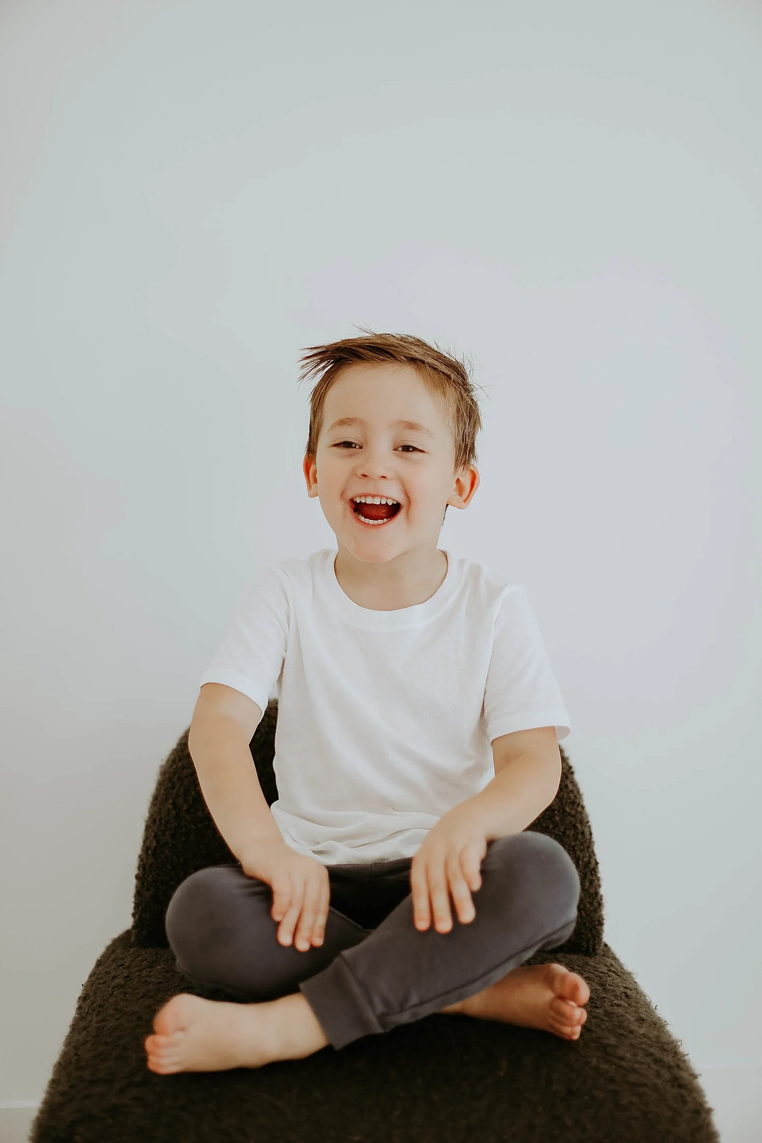  little boy in white shirt sits in chair in studio by Austin family photographer 