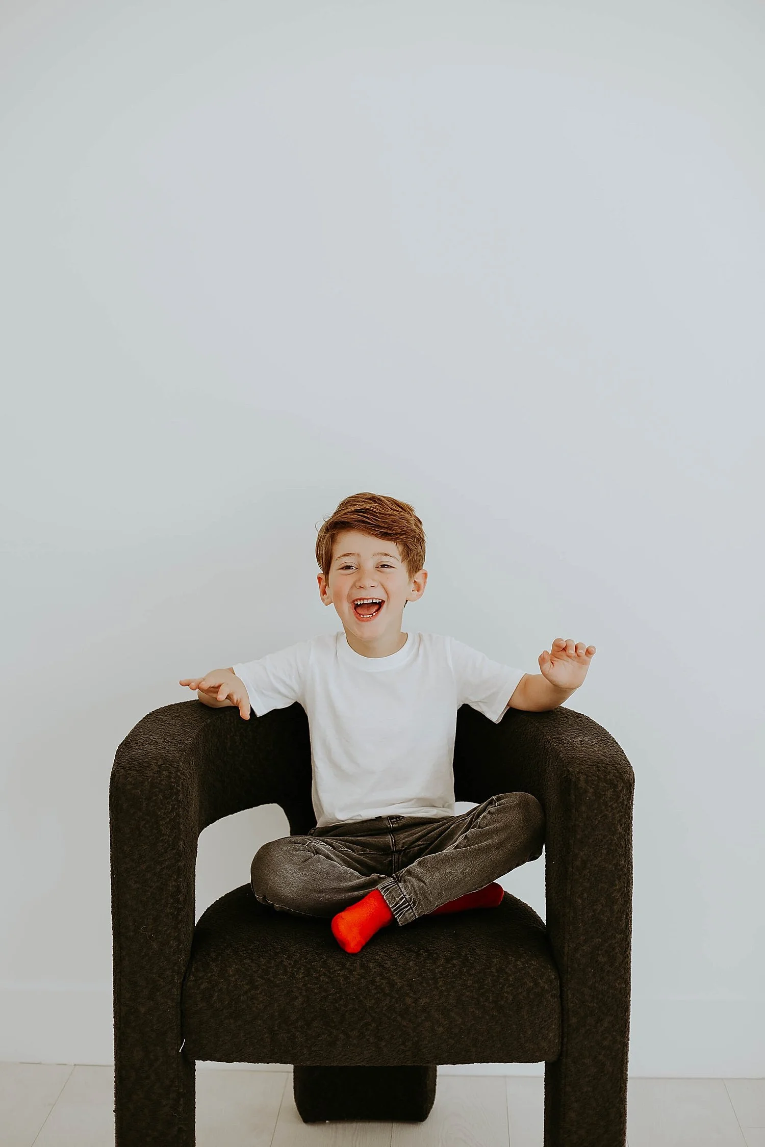  little boy in white shirt laughs in chair for Superhero Best Friend Shoot 