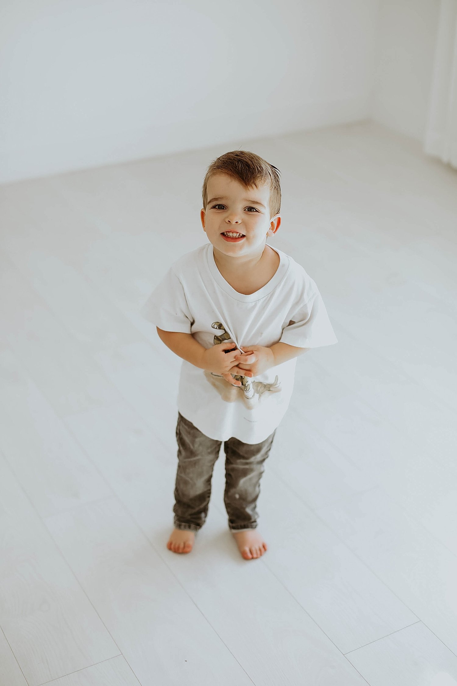  little boy in vintage winnie the pooh shirt stands in white backdrop by Austin family photographer 