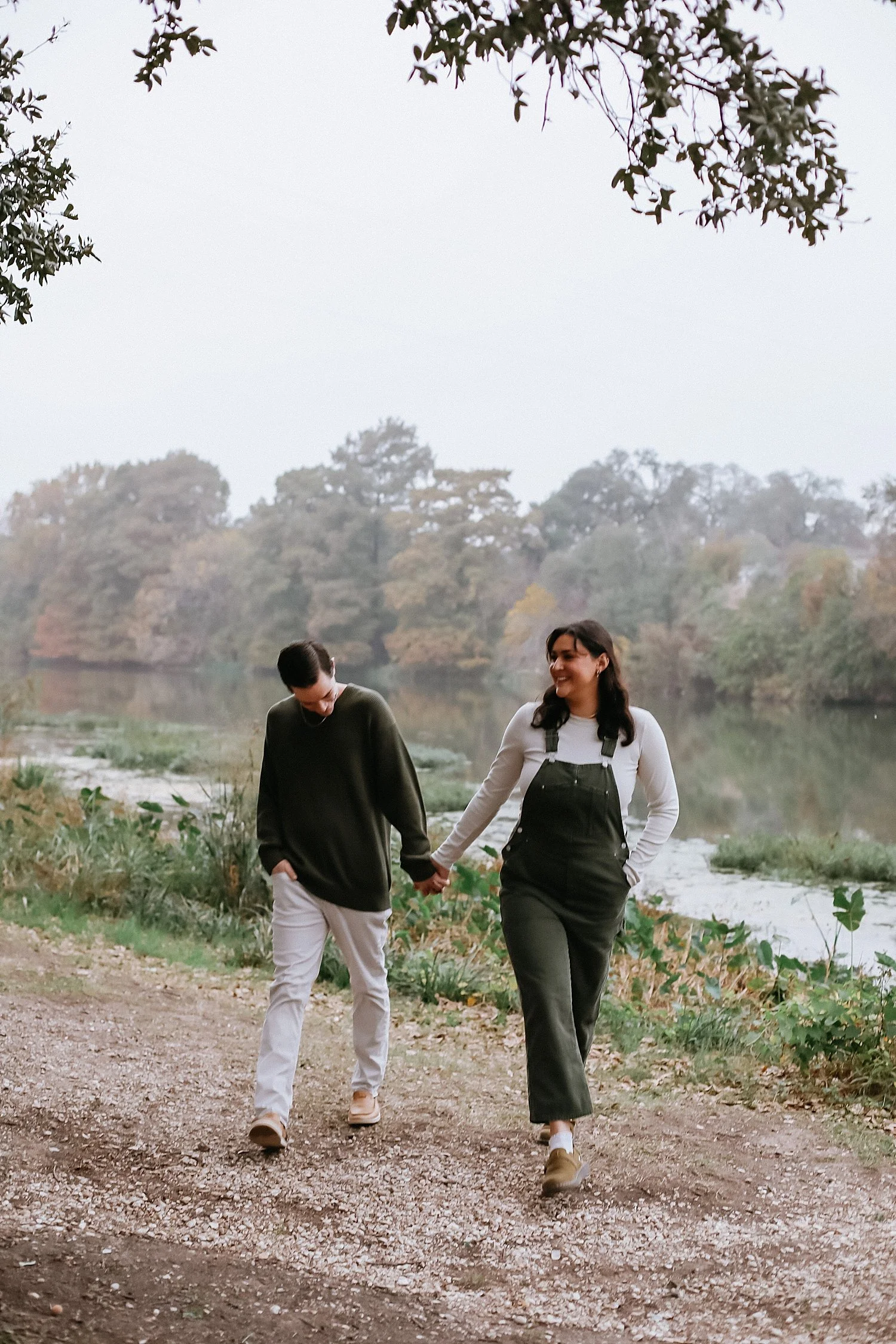  husband and wife walk together alongside creek for overcast fall session 