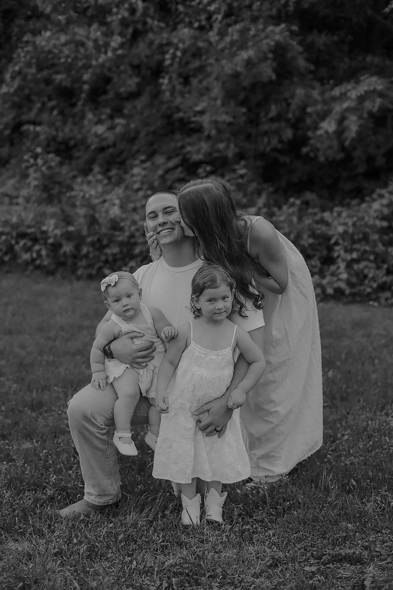  woman kisses her husband while kids sit on his lap for Spring family session 