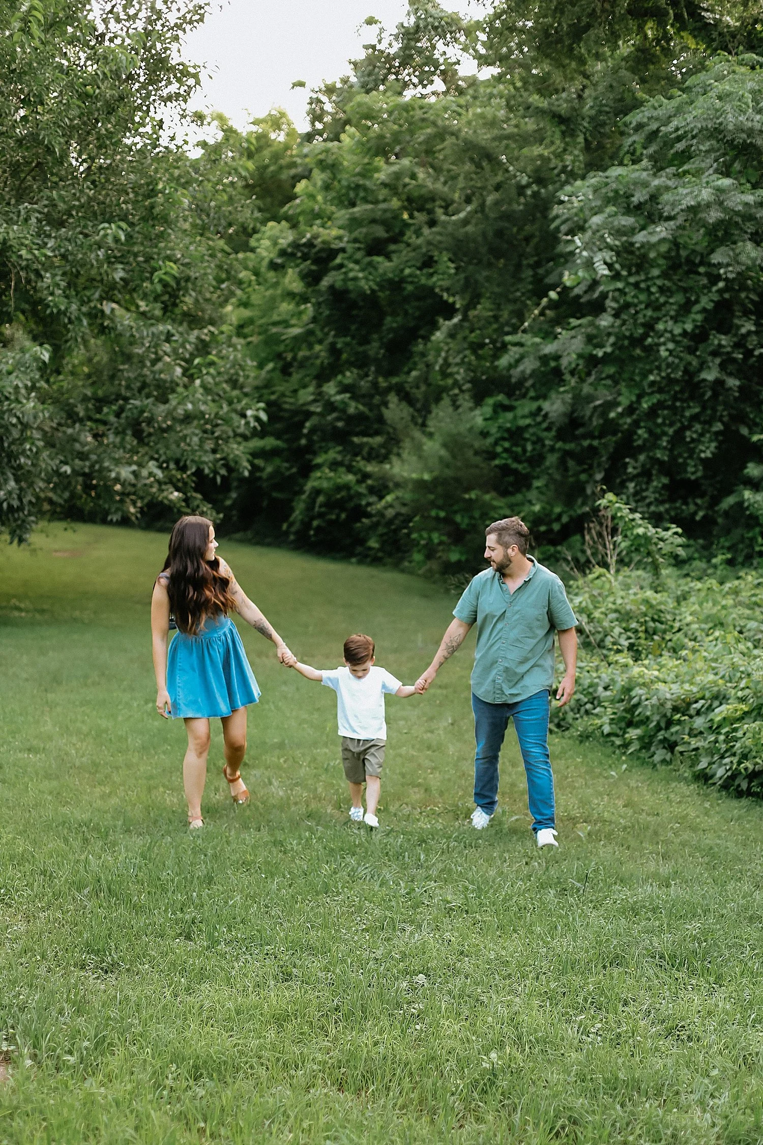  parents walk hand in hand with their toddler through grass by Jessie Shaw Photo 