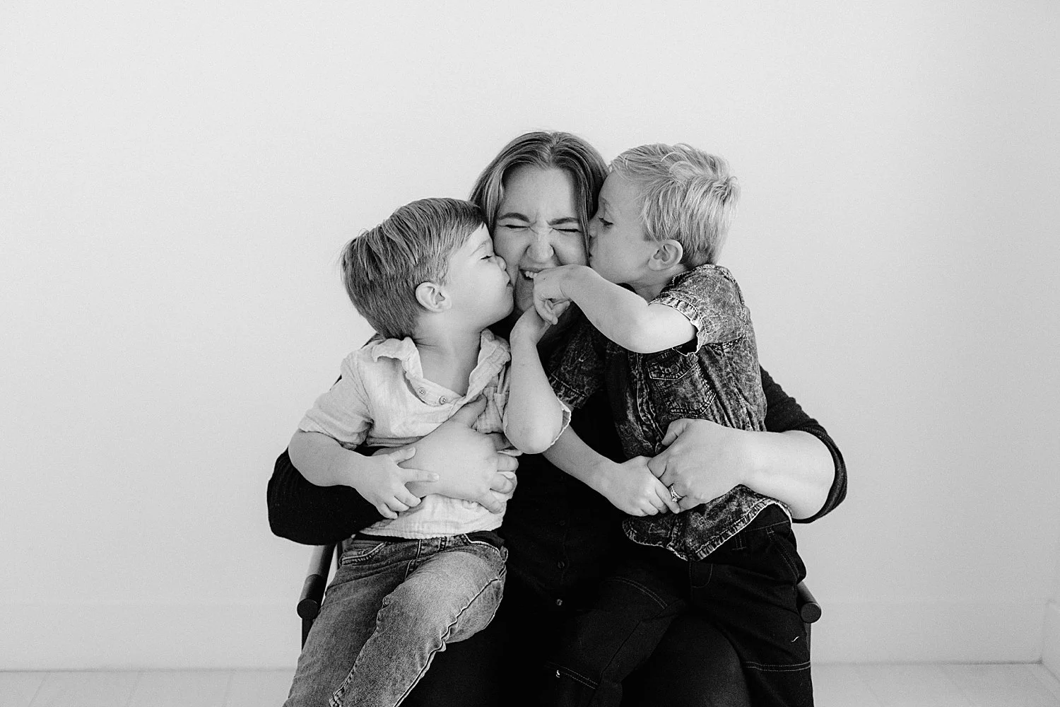  mother holds her little boys in chair while they kiss mom’s cheeks by Jessie Shaw Photo  