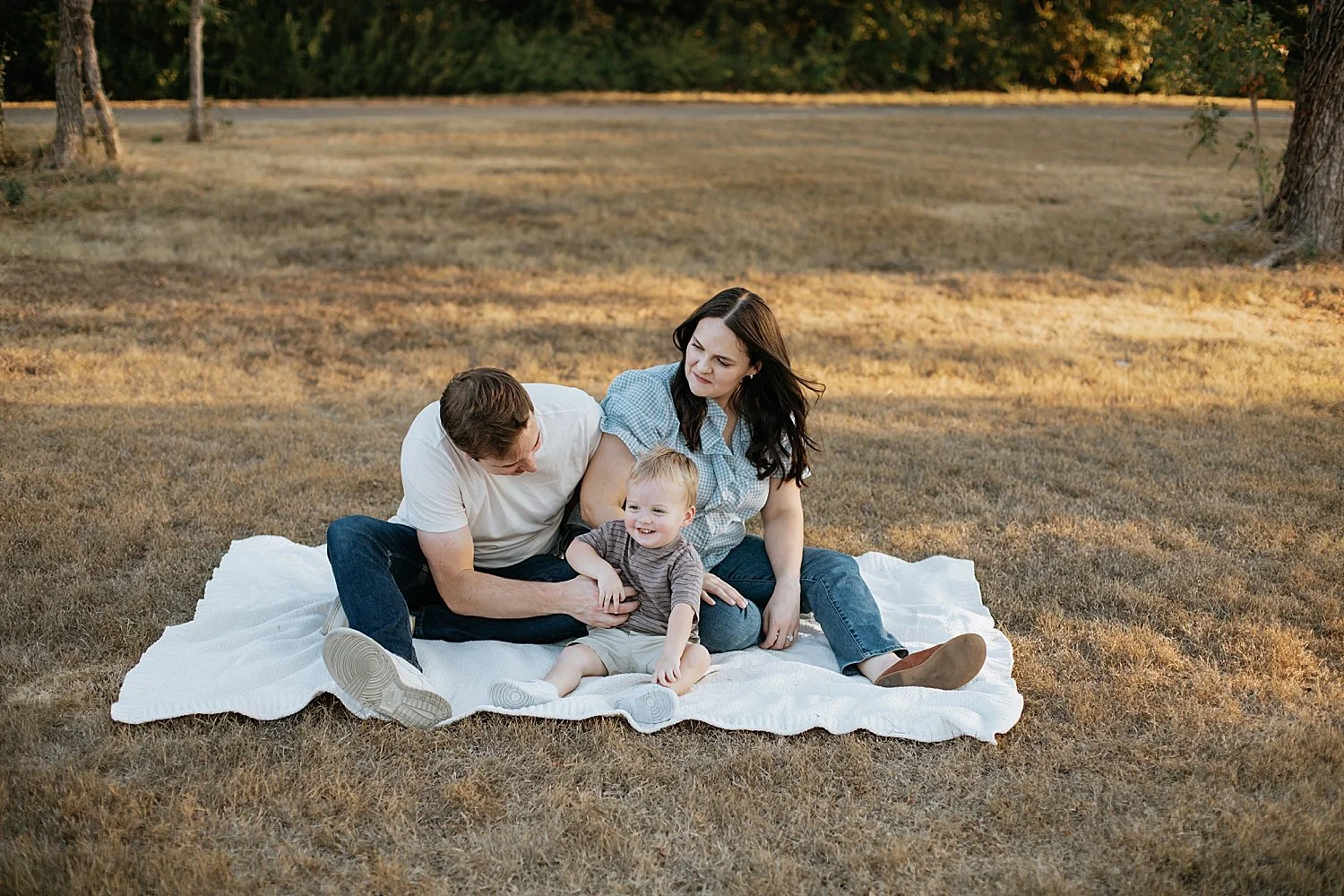  mom and dad play with little one on white blanket by Jessie Shaw Photo 