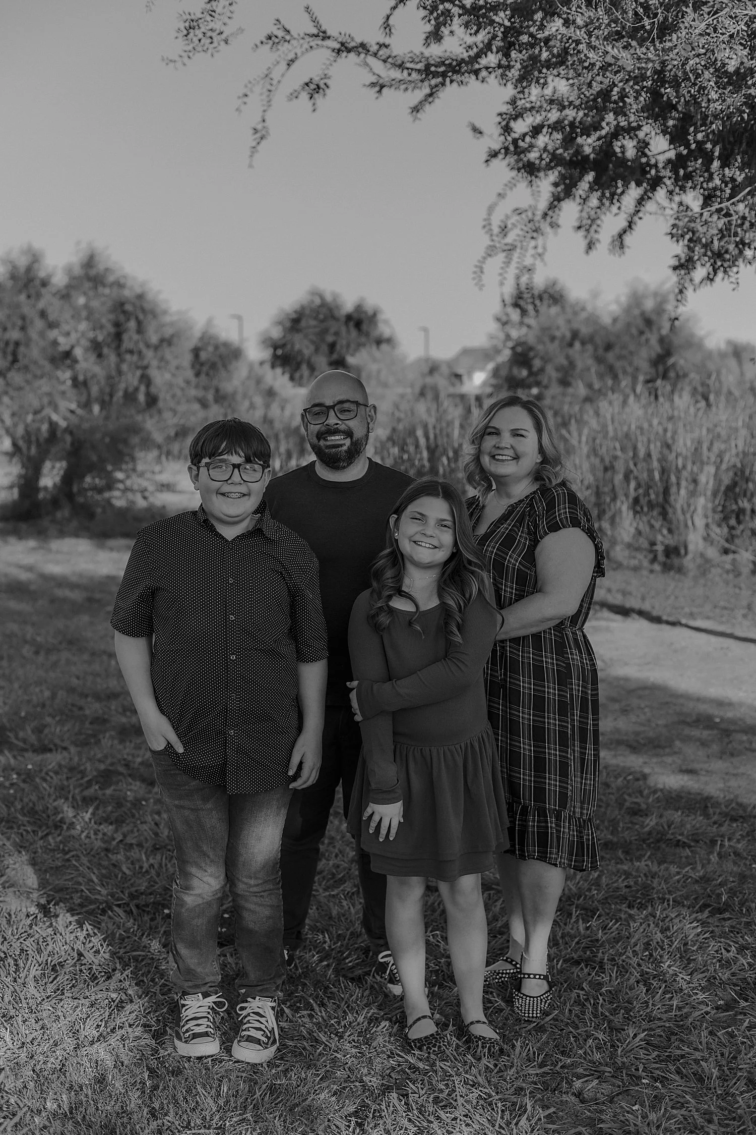  parents stand with their kids under a tree for photos at Lake Pflugerville 