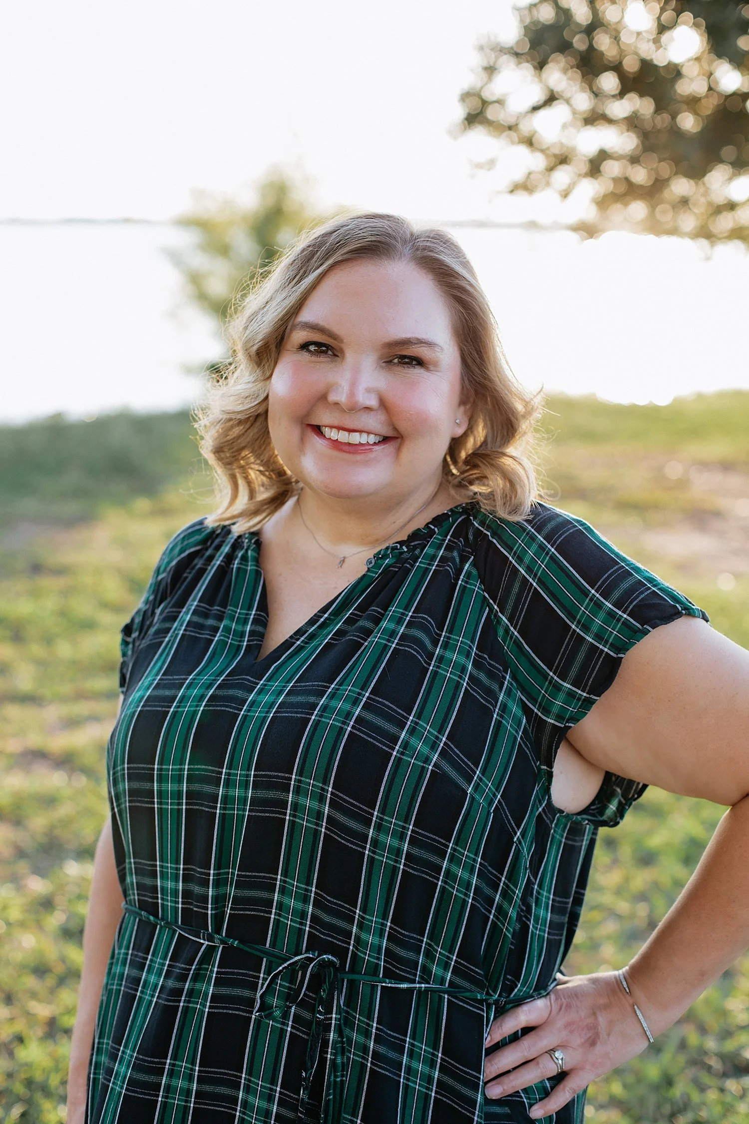  mom in plaid dress stands next to water for photos at Lake Pflugerville 