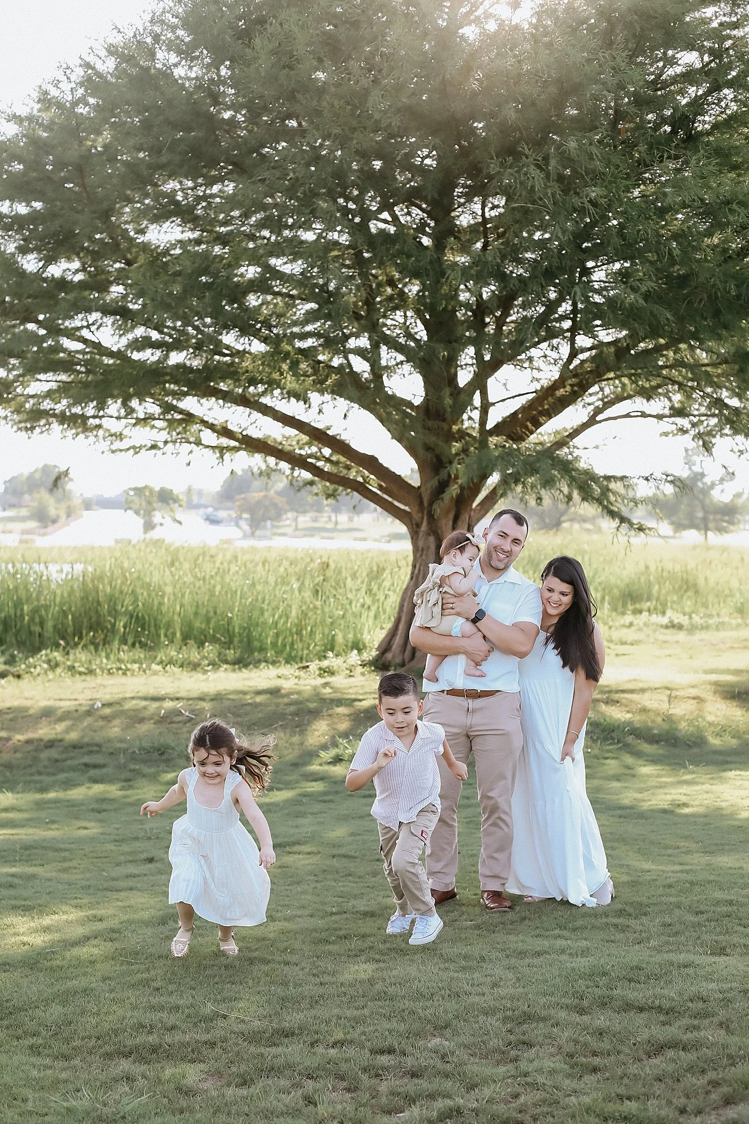  parents stand under big tree while their kids run and play by Jessie Shaw Photo 