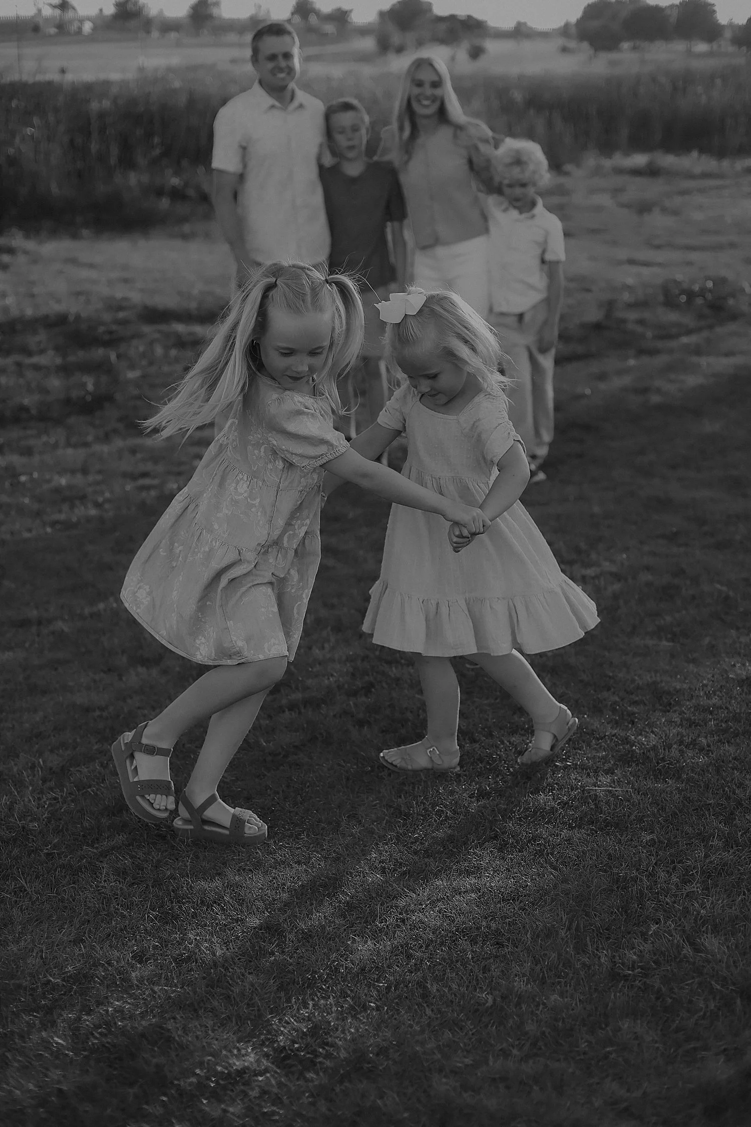 two small girls spin together in field by parents by Jessie Shaw photo