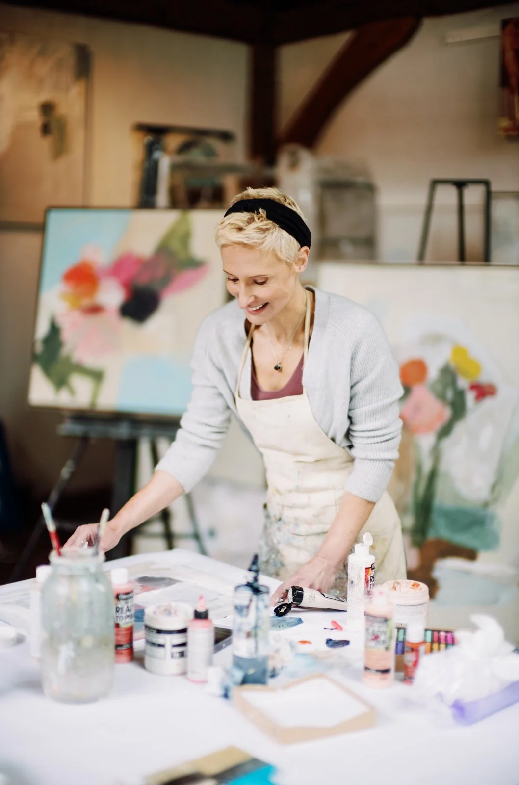 Katie Re Scheidt painting at a worktable with floral paintings in the background