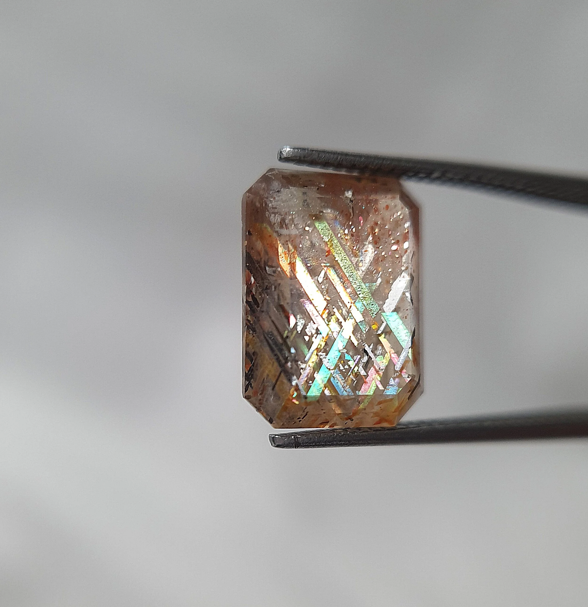 Polished piece of rainbow lattice held between tweezers