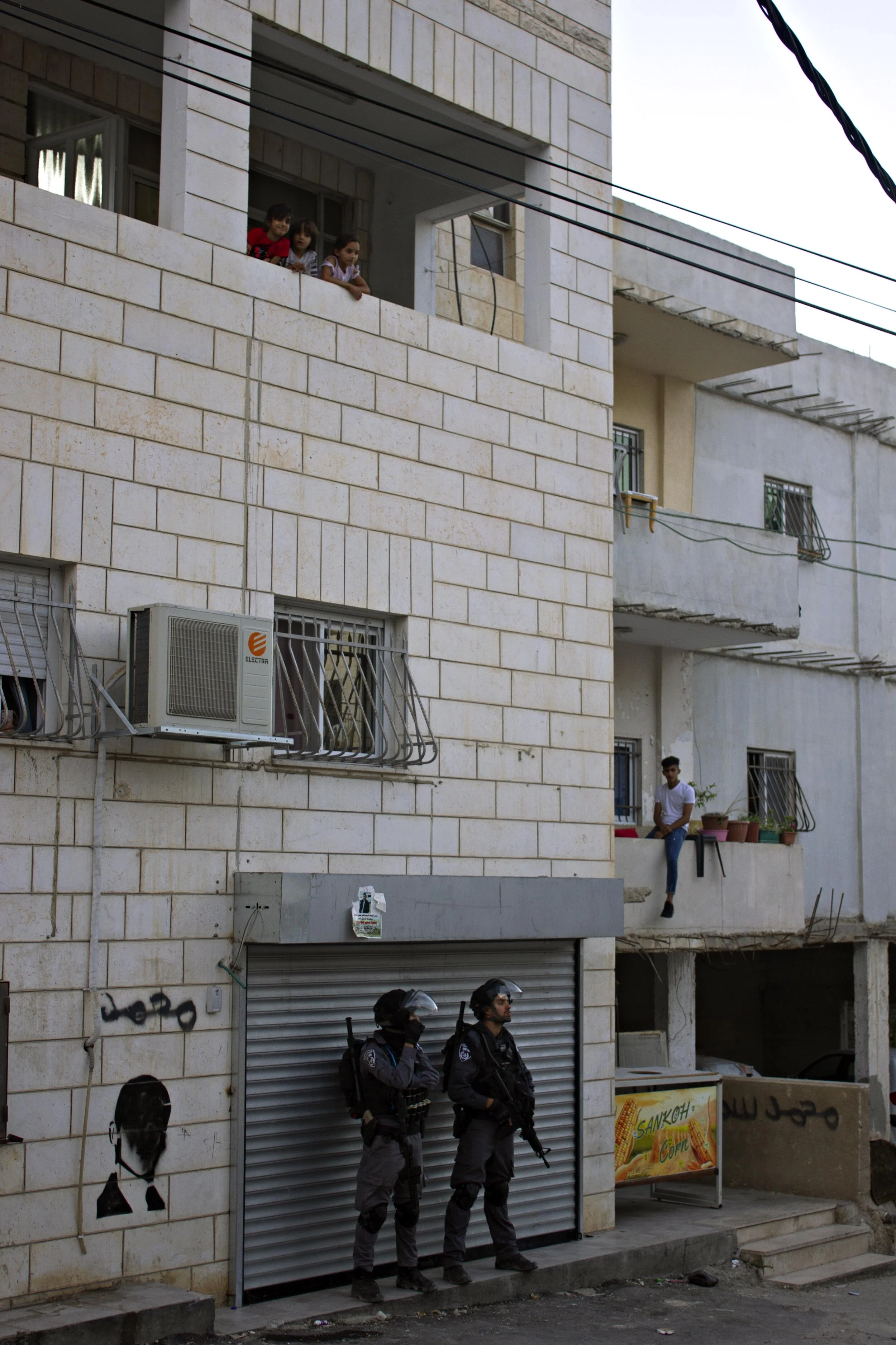 Children look at the camera and police stand on the street.
