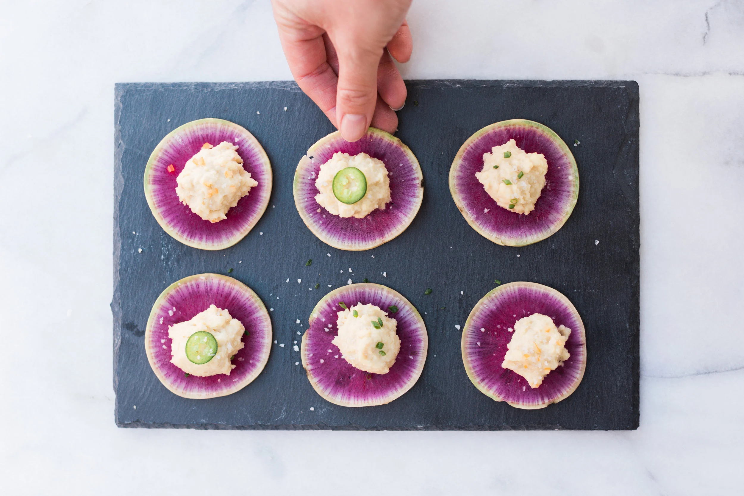Bowl of Tepary Bean Hummus served with sliced watermelon radish and pickled vegetables.