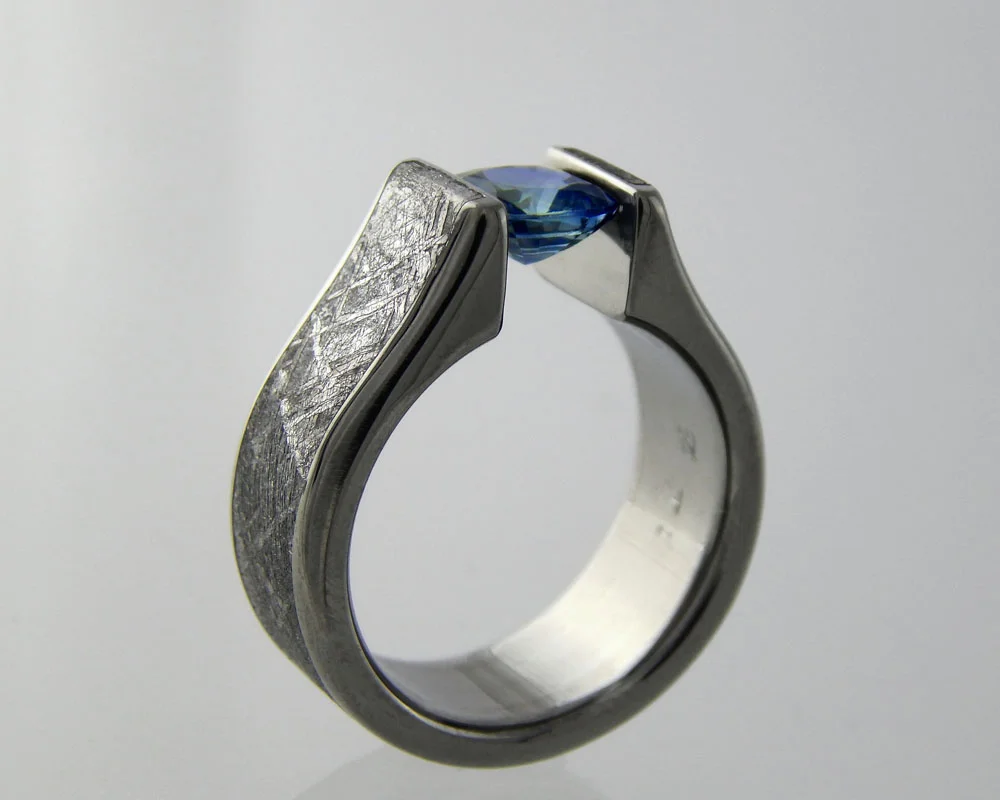 Tension settings - 3D printed titanium rings built to the exact needs of the gem it's holding securely using the memory of the metal to keep it in place. This one is built with a gibbeon meteorite inlay. We recommend moissanite or created sapphire for daily wear.