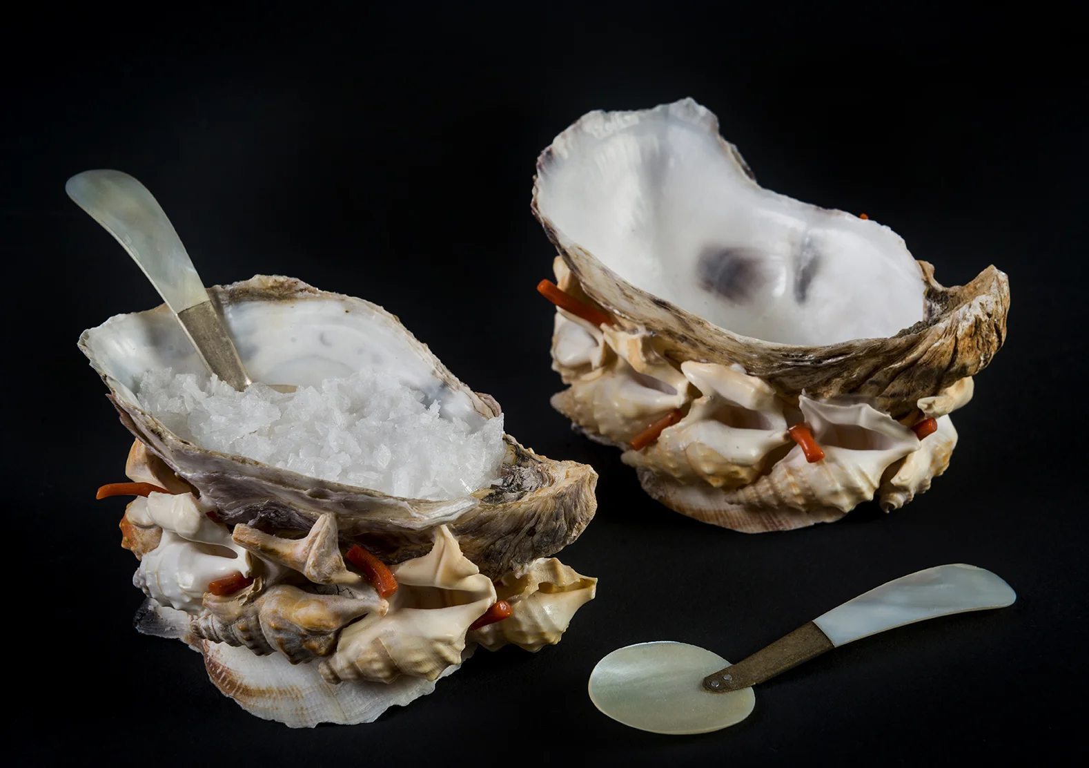 A Pair of Oyster SaltsA pair of oyster shell salts with interlocking pelican shells and fragments of antique, red, polished corals around the base. Two miniature mother-of-pearl spoons included. 10cm x 5cm