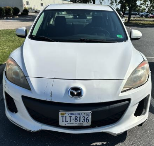 Front view of a white Mazda sedan showing the emblem, hood scratches, headlights, and front license plate.