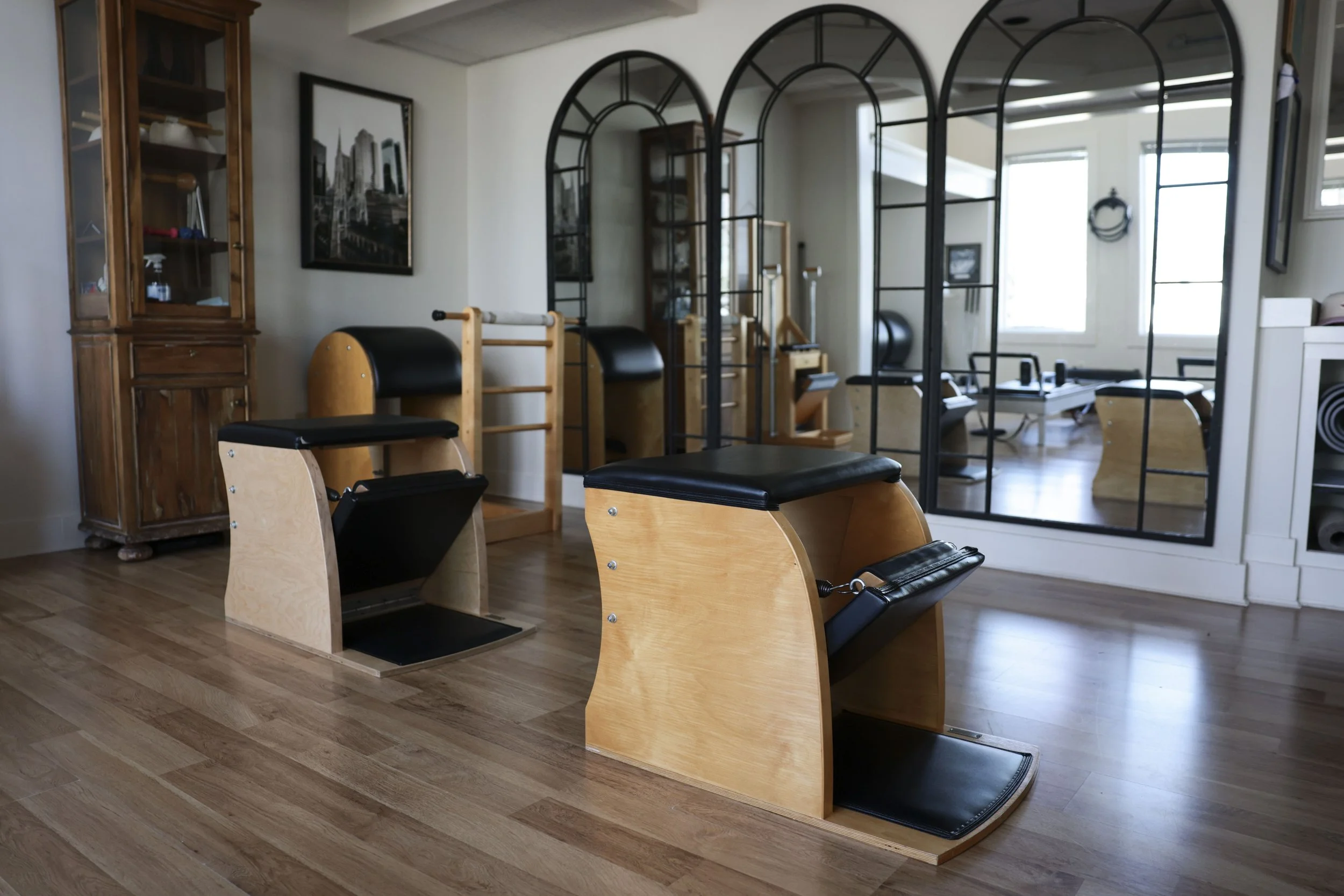 Pilates reformer machines in a fitness studio with wooden floors and large mirror dividing the space.