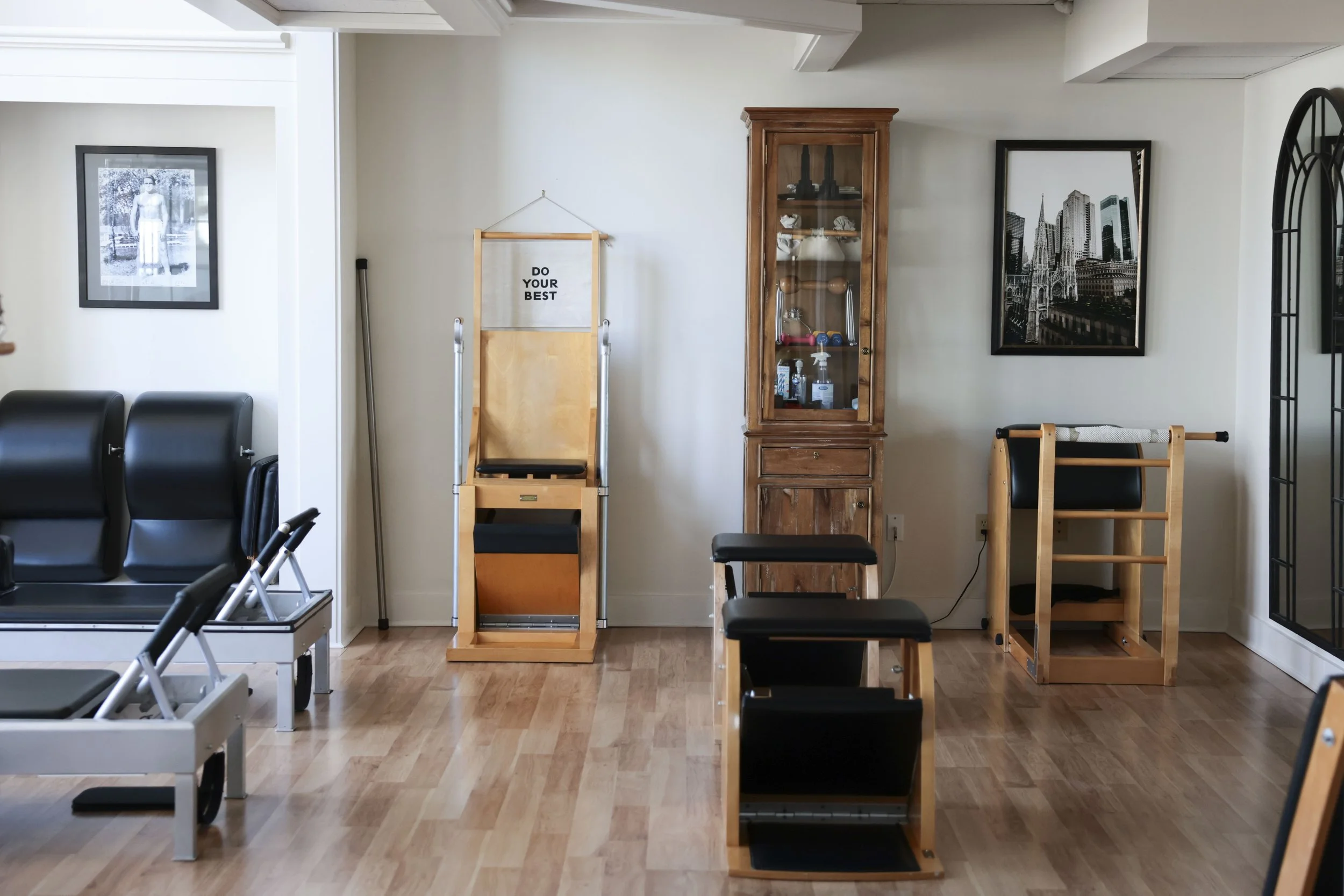 A room with various exercise equipment and framed artwork on the walls, including a black and white photo of a woman, a cityscape print, and a motivational quote on a hanging banner that says 'Do Your Best.'