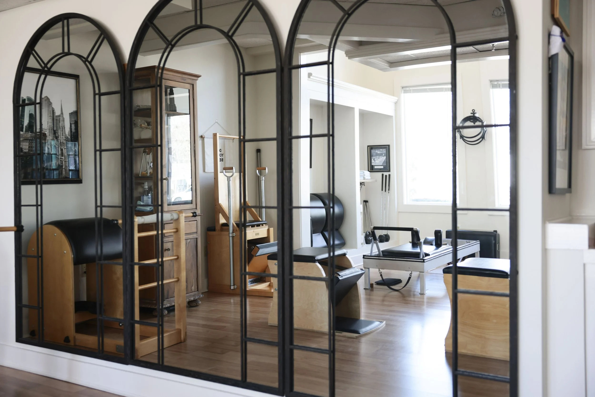 Interior of a Pilates or fitness studio with workout equipment visible through a decorative black metal framed mirror.