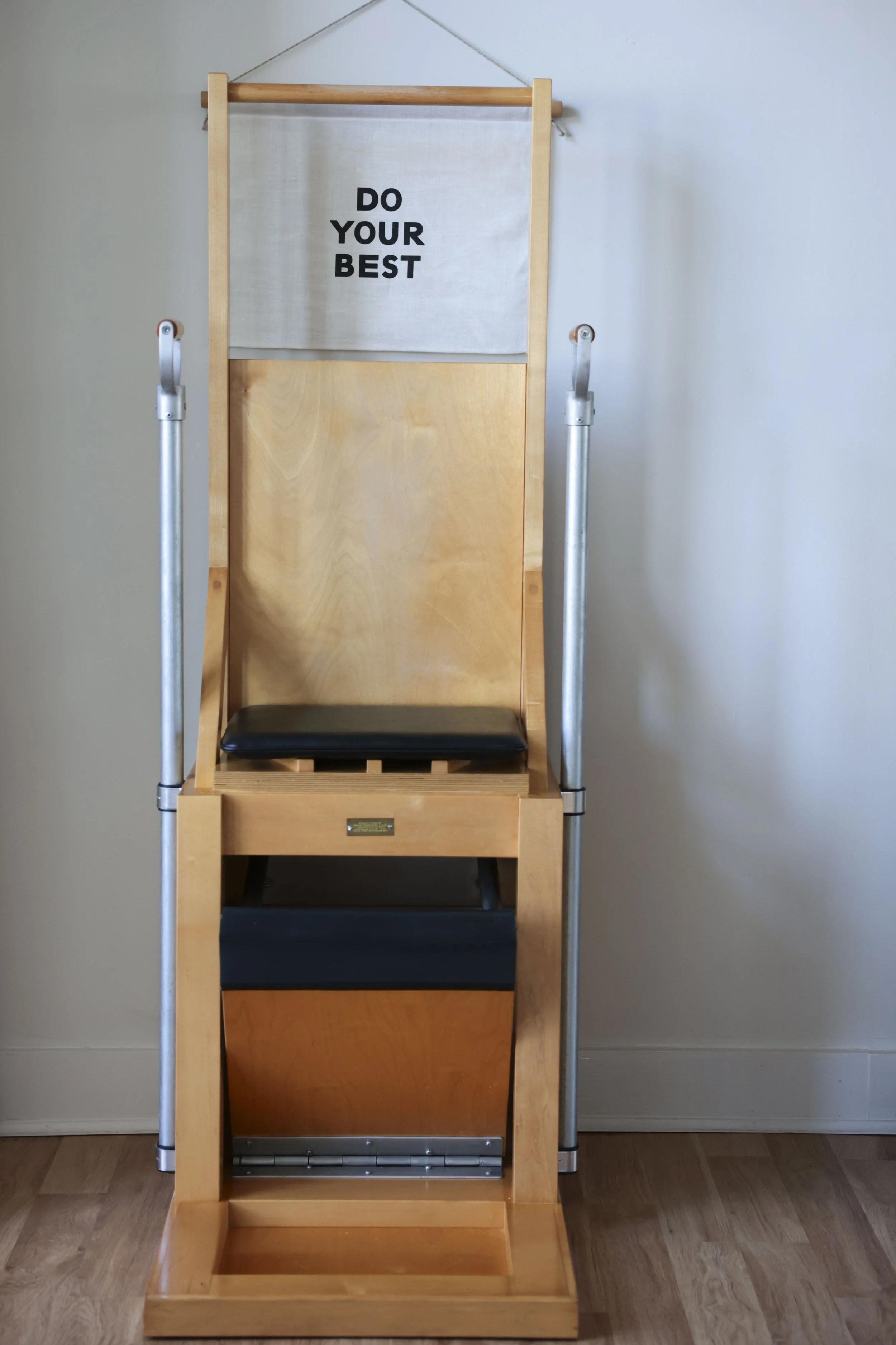 A wooden inversion table with a black padded seat and a fabric panel at the top displaying the message "Do your best."