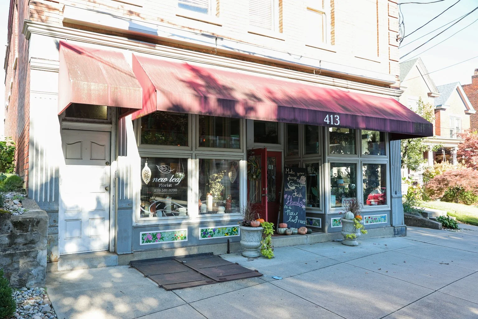 The exterior of A New Leaf in Newport, Kentucky. There is a red awning that displays the numbers 413 for the address. There is a white decal on the window that says A New Leaf. There is a chalkboard sign propped open on the porch