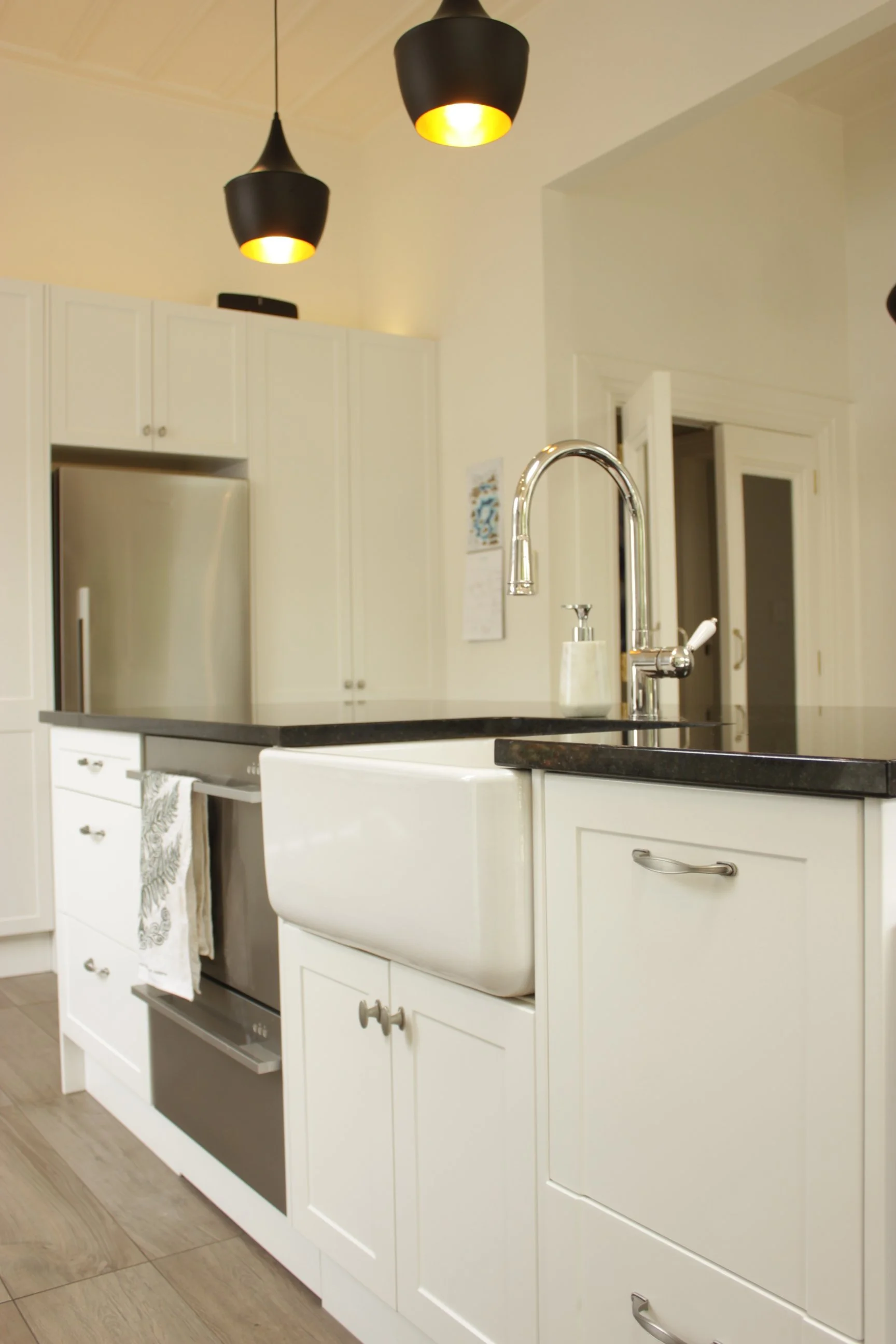 Modern kitchen renovation featuring white cabinets, stainless steel appliances, farmhouse sink, black countertop, pendant lighting.