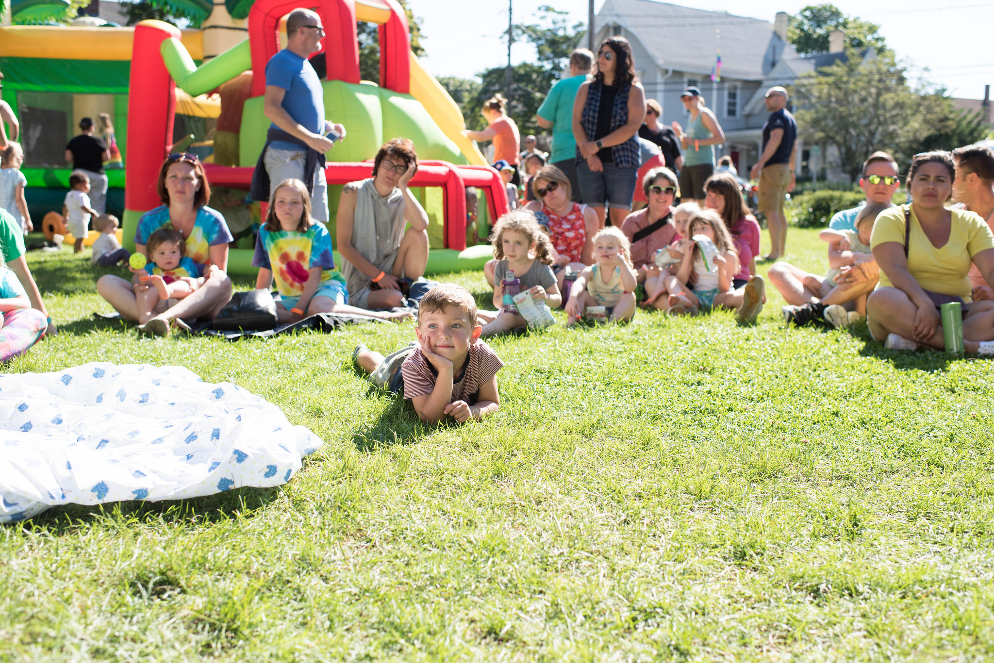 A group of families sitting on grass in front of a bouncehouse at Littles