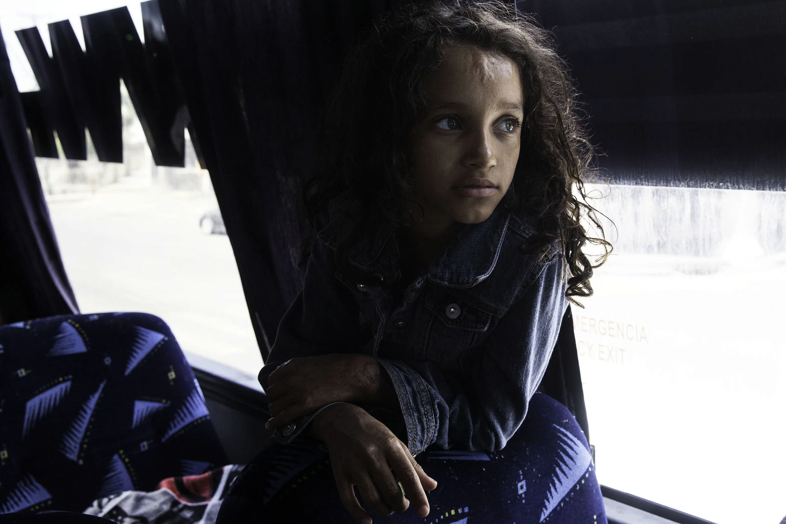 A young girl with burn marks from Central America watches television while people board a bus that is headed to Tijuana, MX on April 24, 2018. The bus stopped in Mexicali, MX, for about two hours while volunteers fed them, medical professionals were available, people were able to charge phones and relax in a big room.
