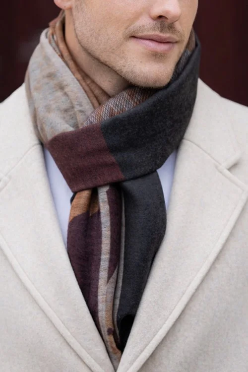 Closeup of a man wearing the natural colour variant of the houndstooth patterned Agnes Scarf made from 100% Merino wool and tied in a loose knot under a jacket.
