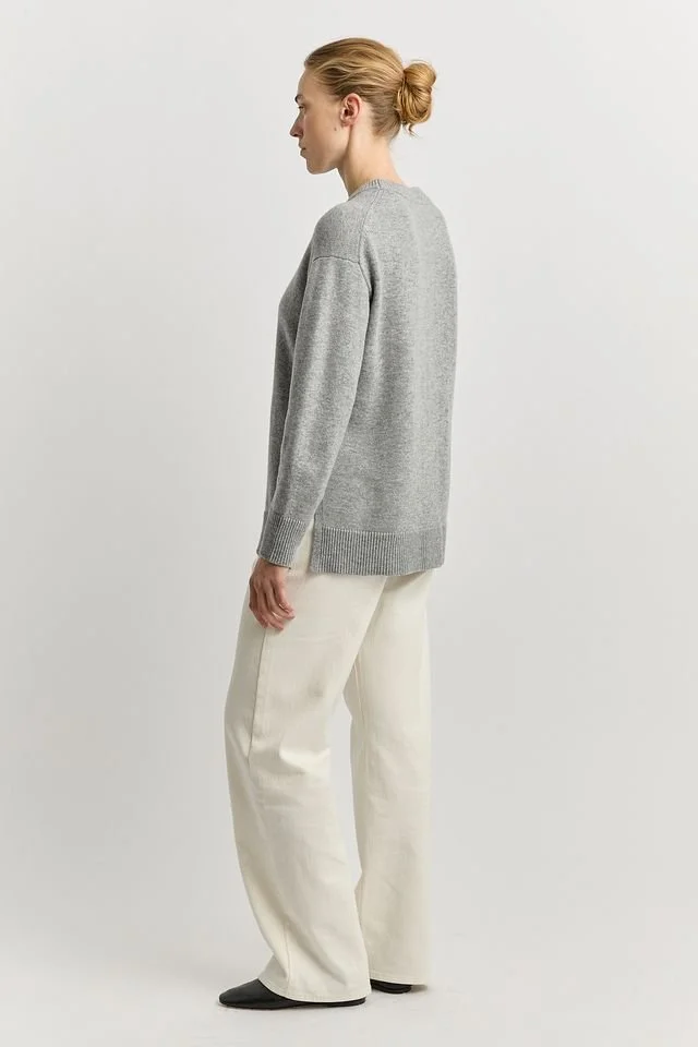 Back view of a woman wearing the Light Ash colour variant of the Toorallie Relaxed Longline Crew Sweater made from 100% Merino lambswool