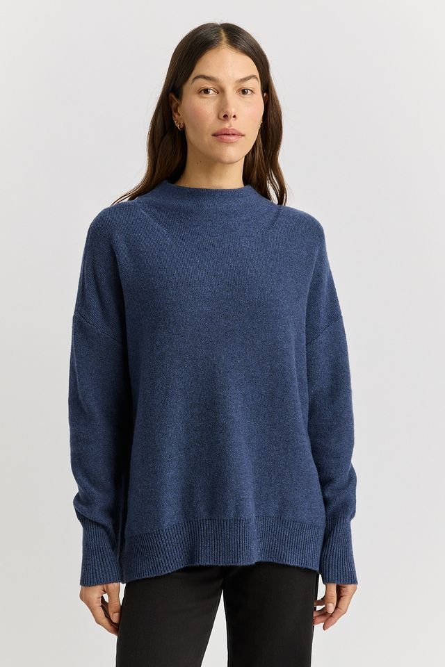 Woman wearing the Galaxy Blue colour variant of the Toorallie Drop Shoulder Mock Neck Sweater made from 100% Merino lambswool)