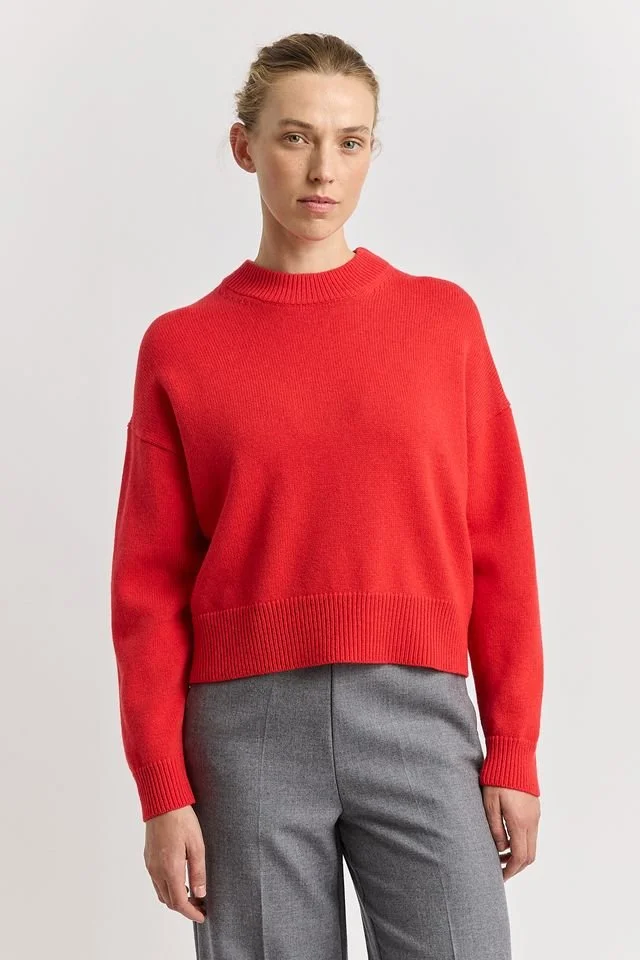 Woman wearing the Poppy red colour variant of the Toorallie Drop Shoulder Crew Neck Sweater made from 100% Merino lambswool)